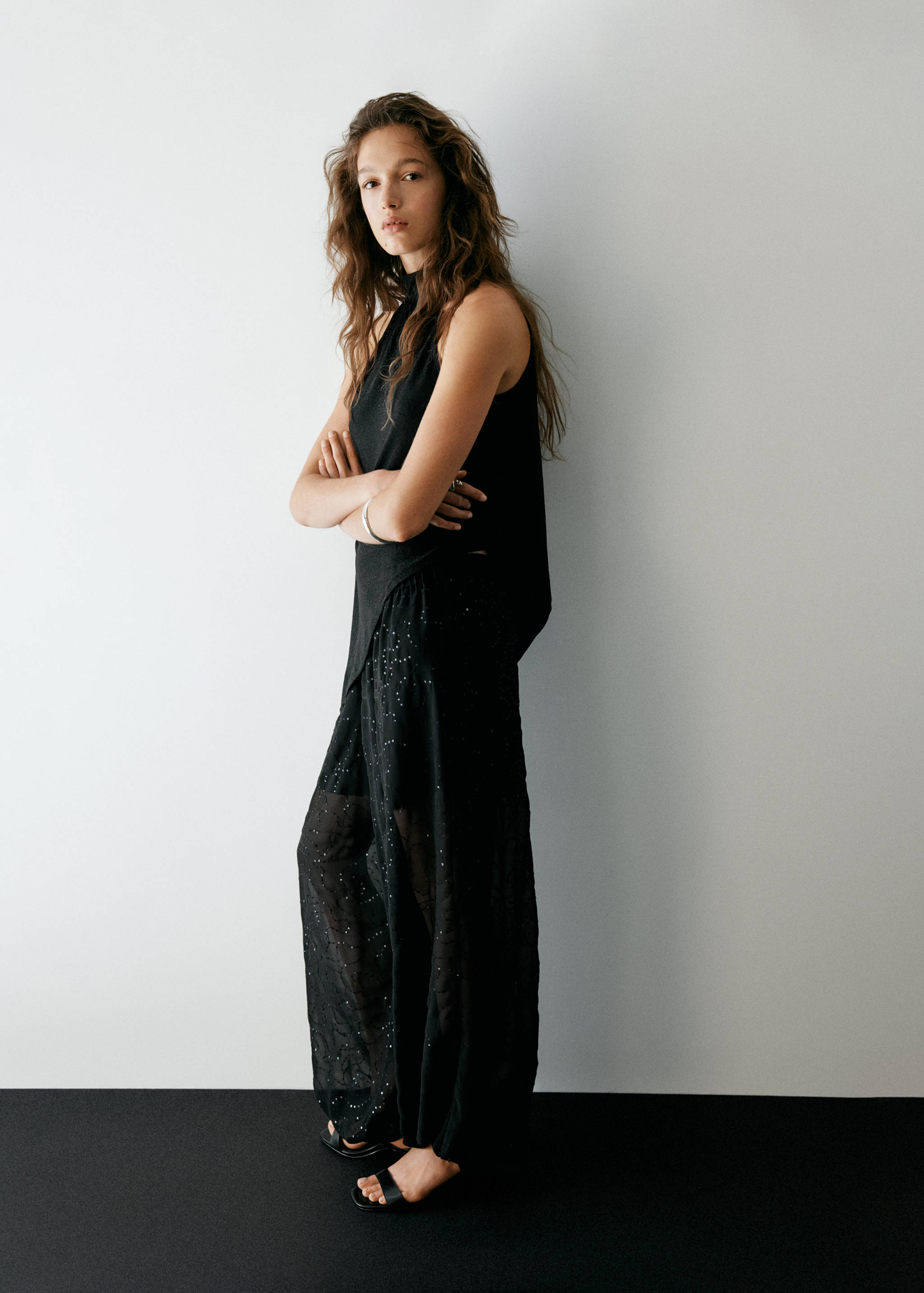Black sleeveless high-neck top worn with black patterned trousers.