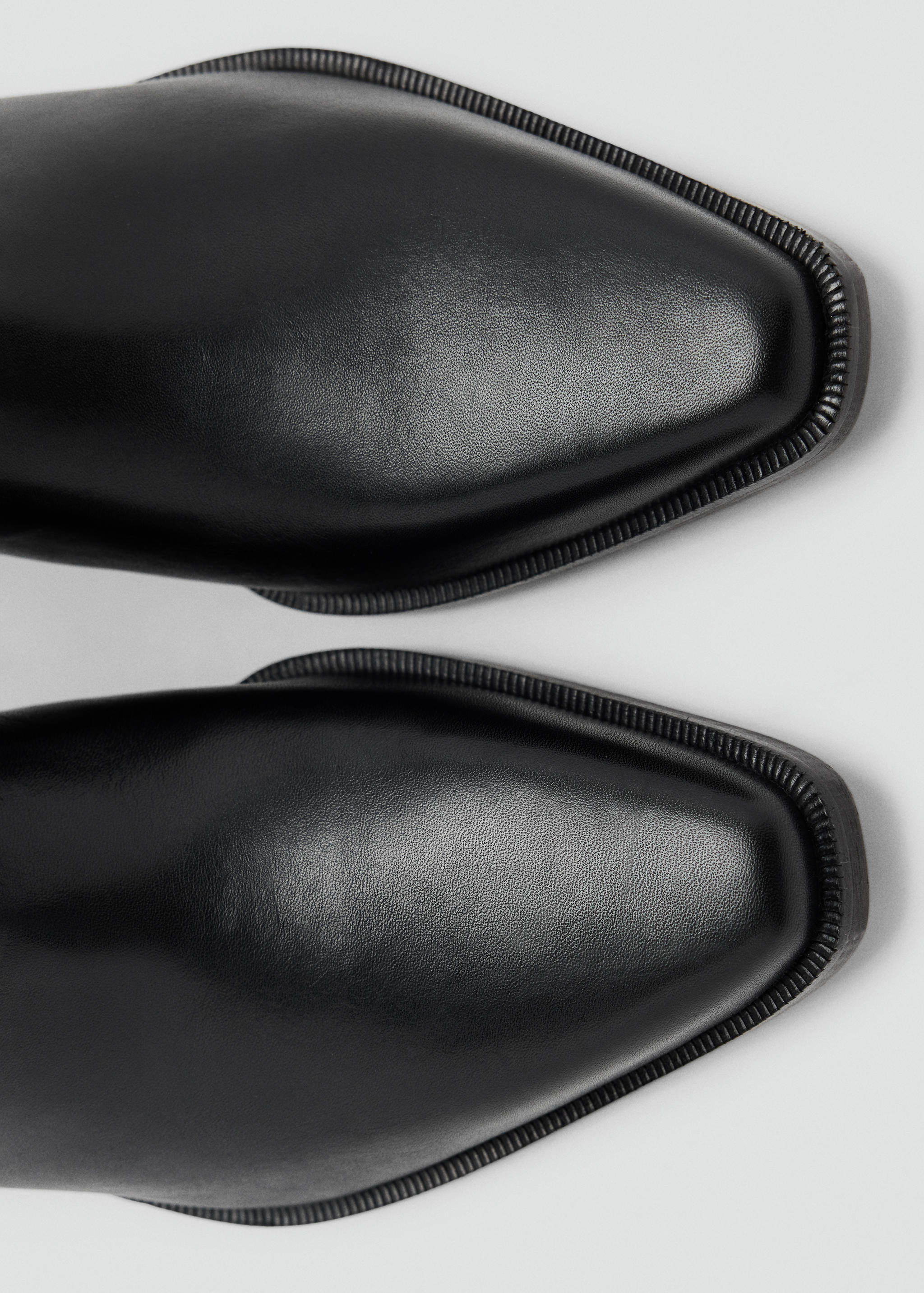 Close-up of black boots featuring a pointed toe with a square tip and welt trim.