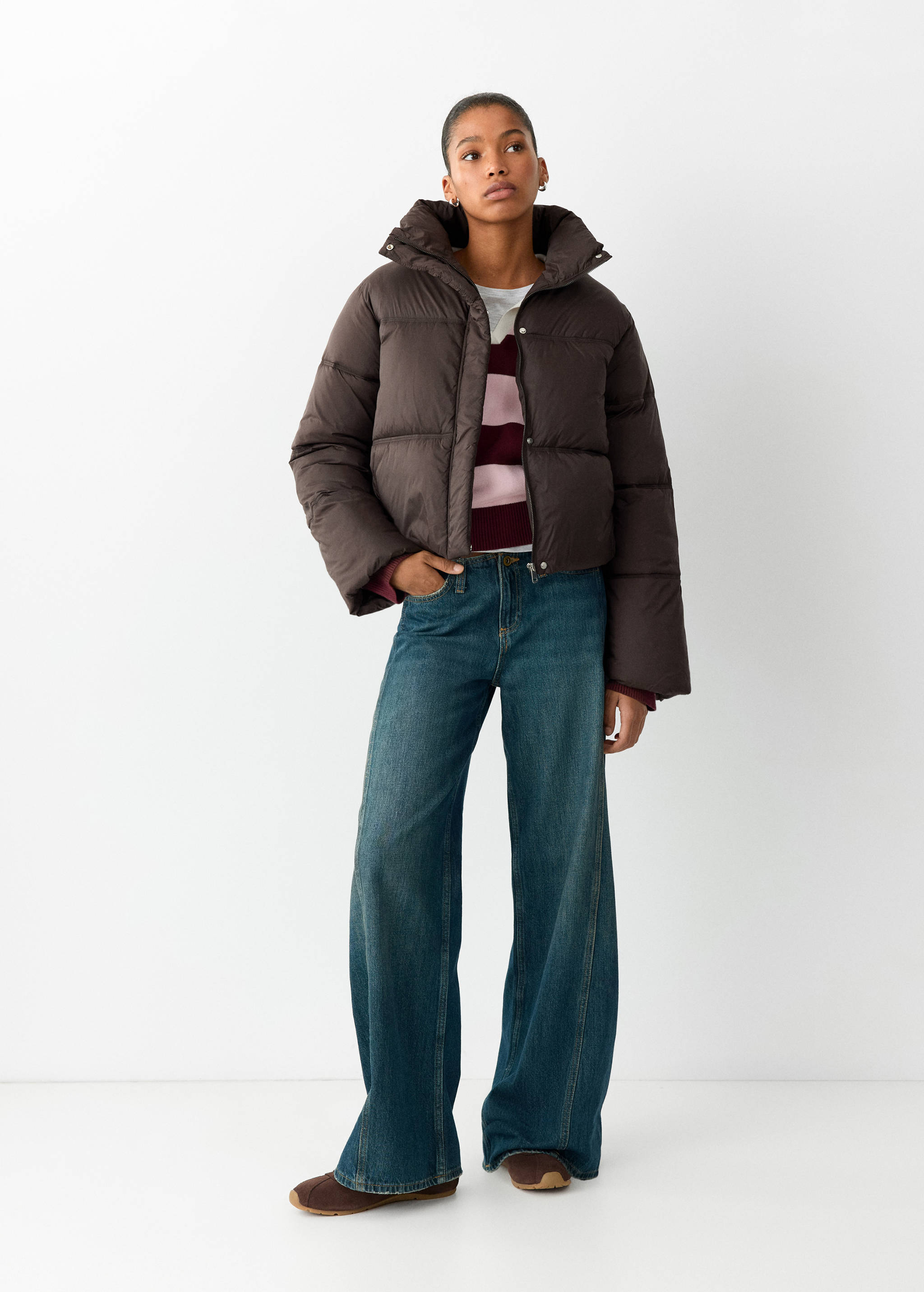 Brown cropped puffer anorak with a high collar, worn with striped top and blue trousers.