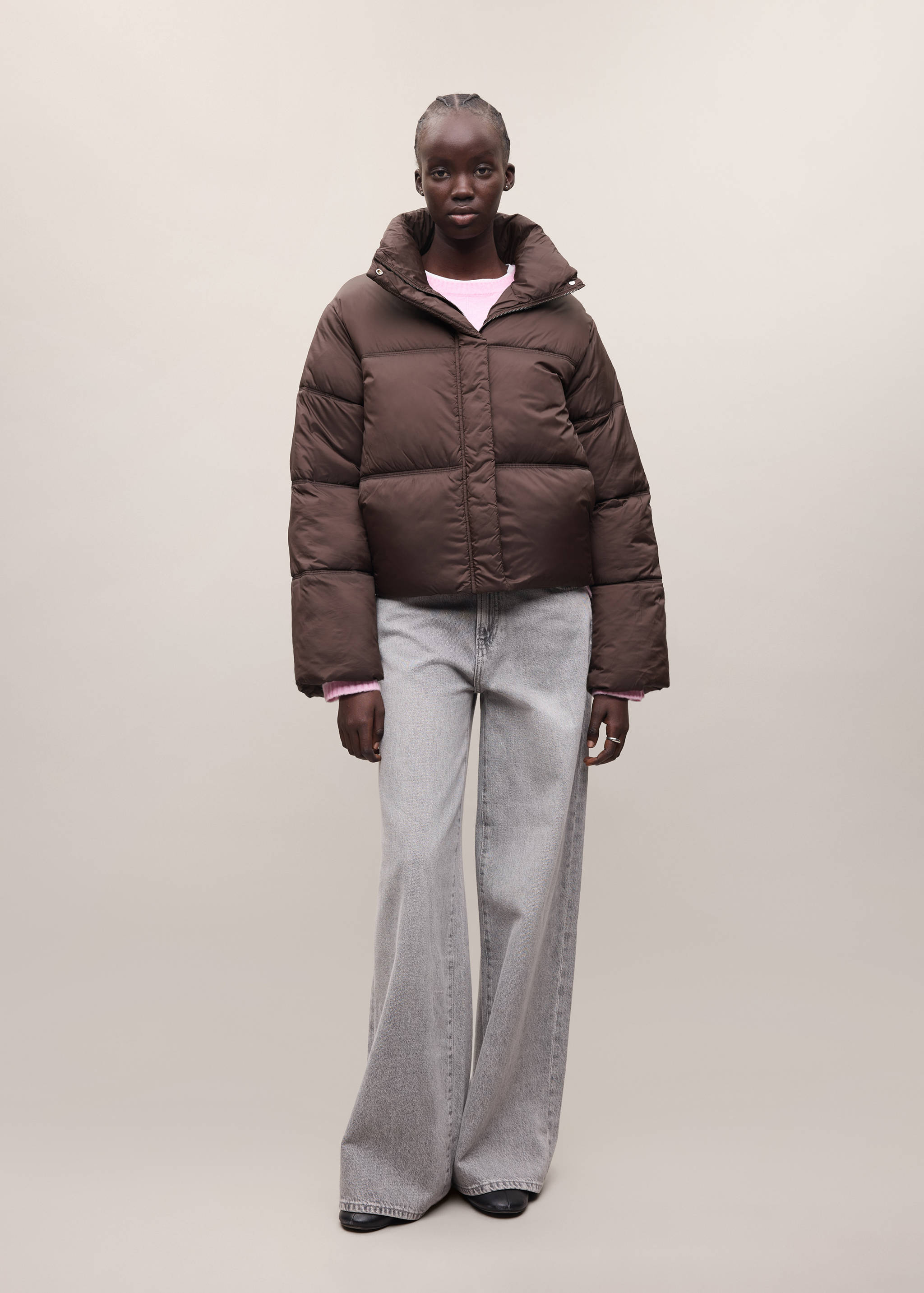 Dark brown quilted puffer anorak with a high collar, worn with a pink sweater and grey wide-leg jeans.