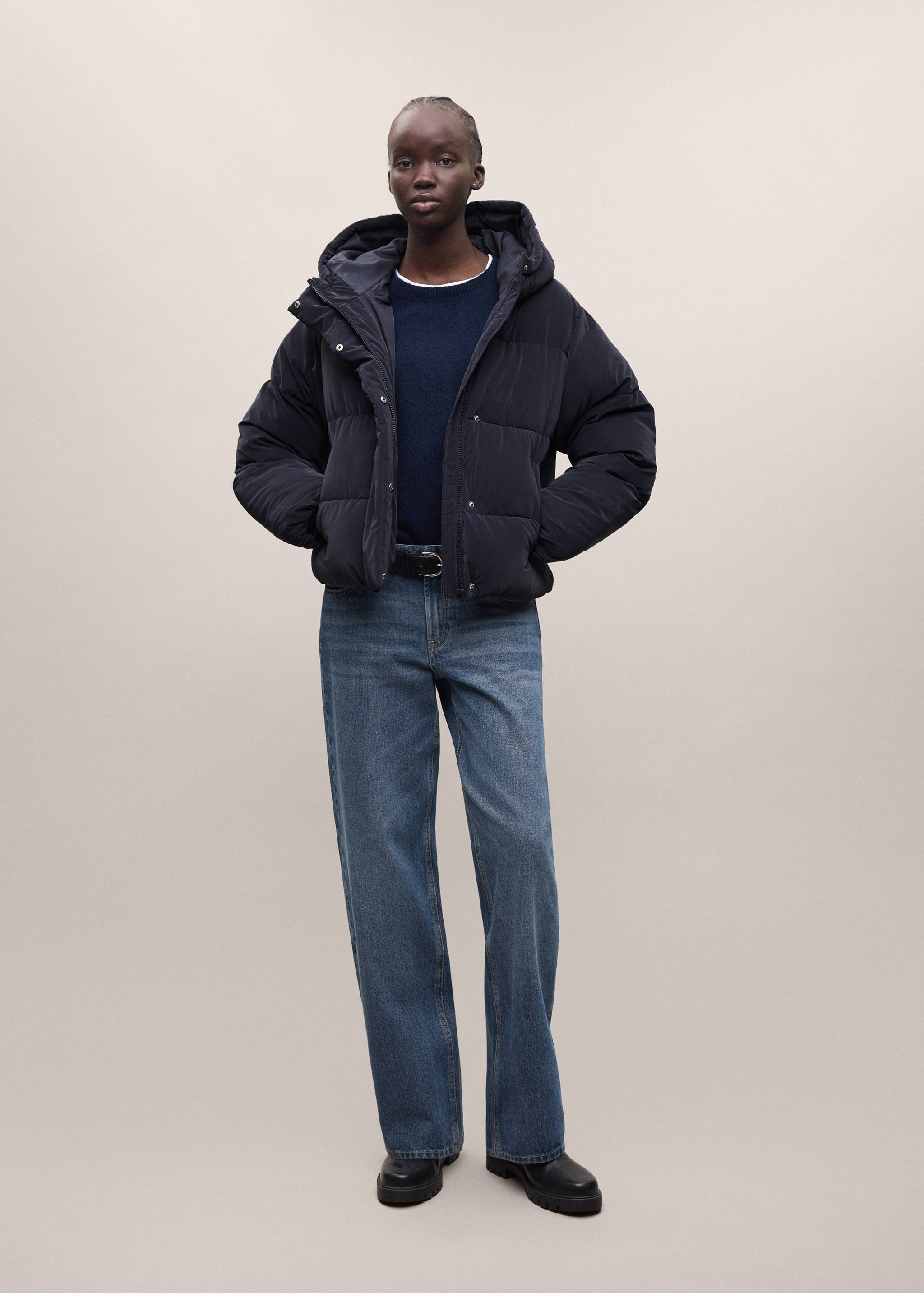 Navy blue quilted anorak with a hood and horizontal baffles, worn with a jumper, blue jeans, and boots.