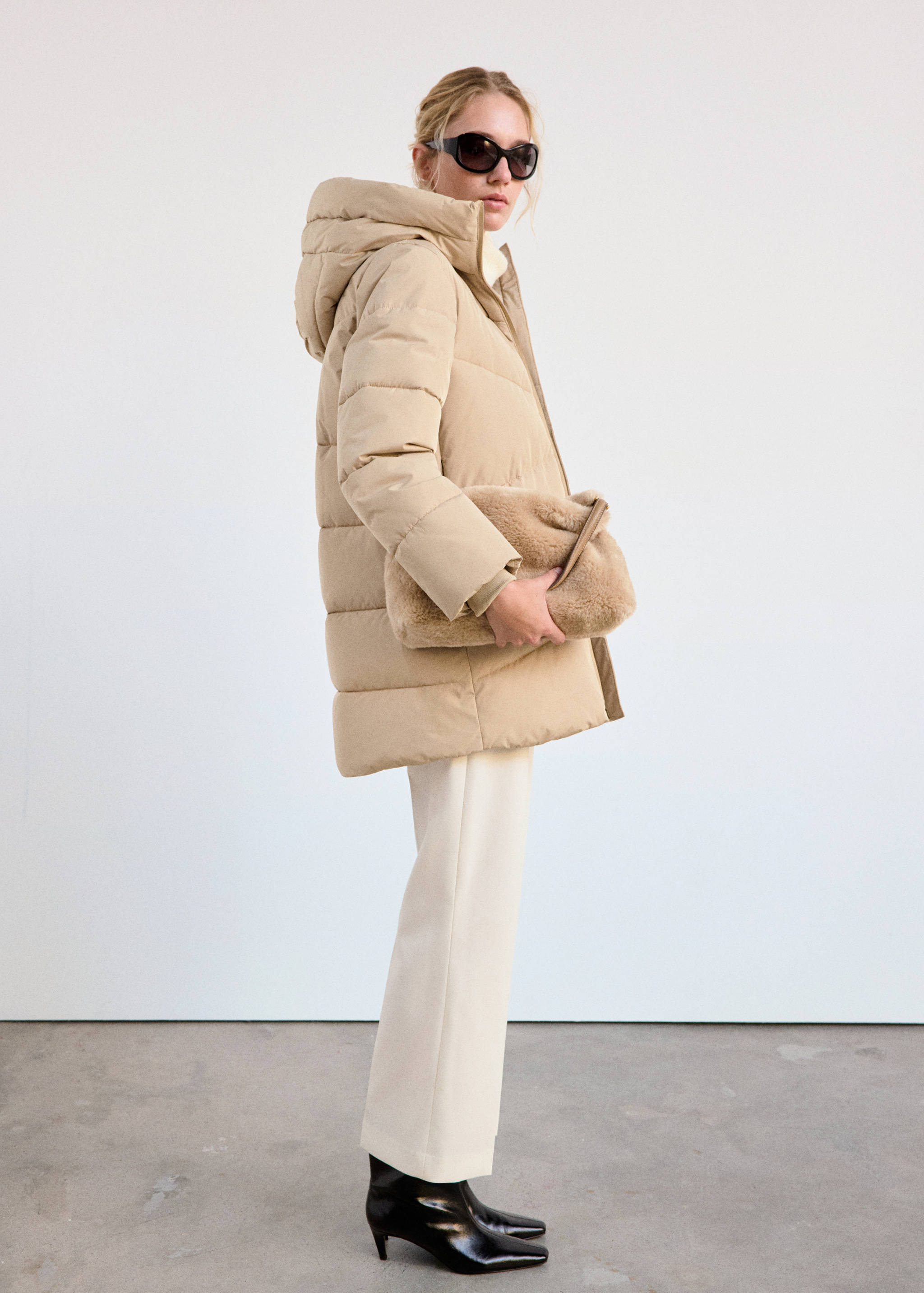 Beige hooded quilted anorak worn with cream trousers and a faux-fur clutch.