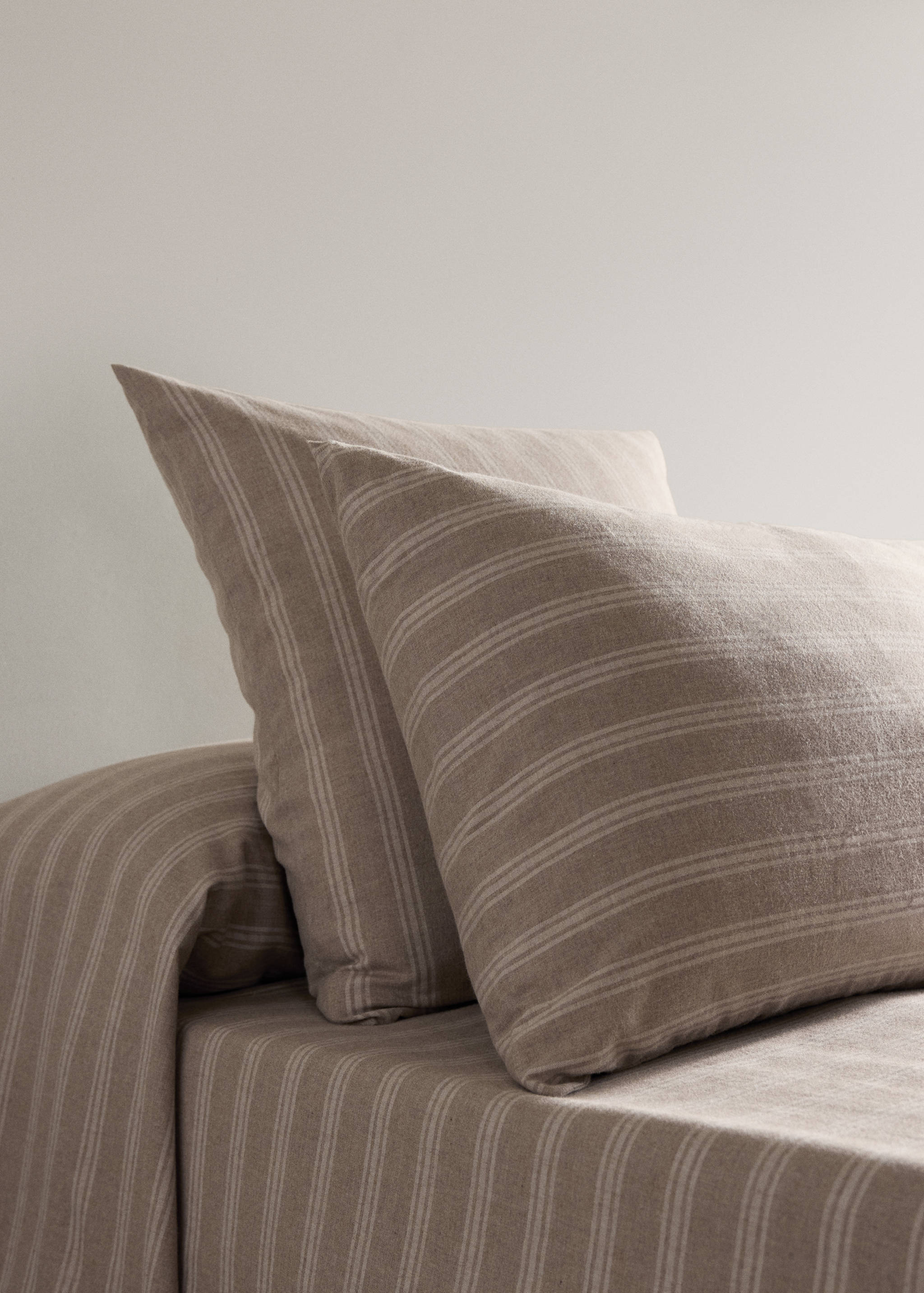 Beige and white striped pillowcase on a made bed