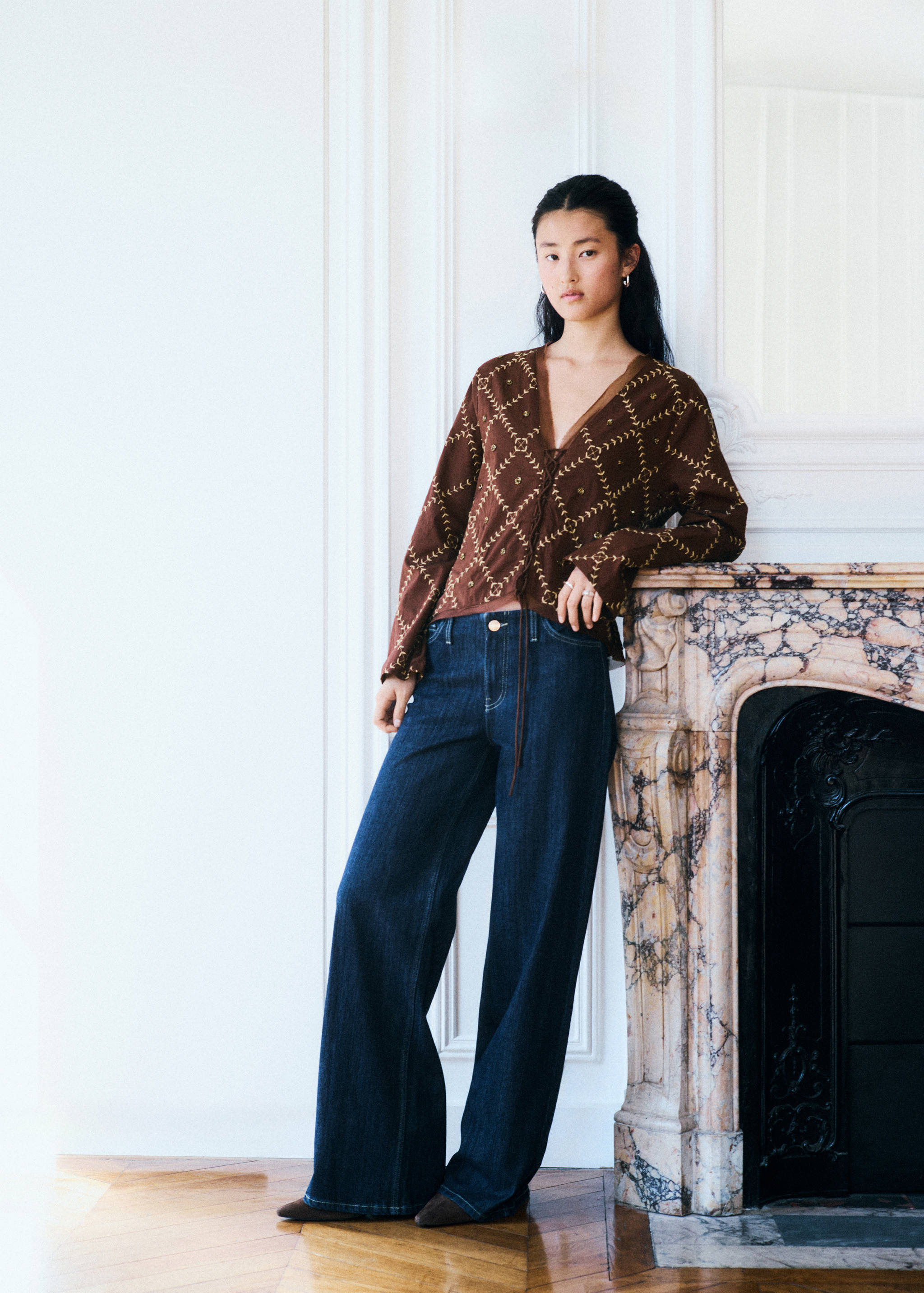 Brown embroidered V-neck top with a front tie, paired with wide-leg denim trousers.