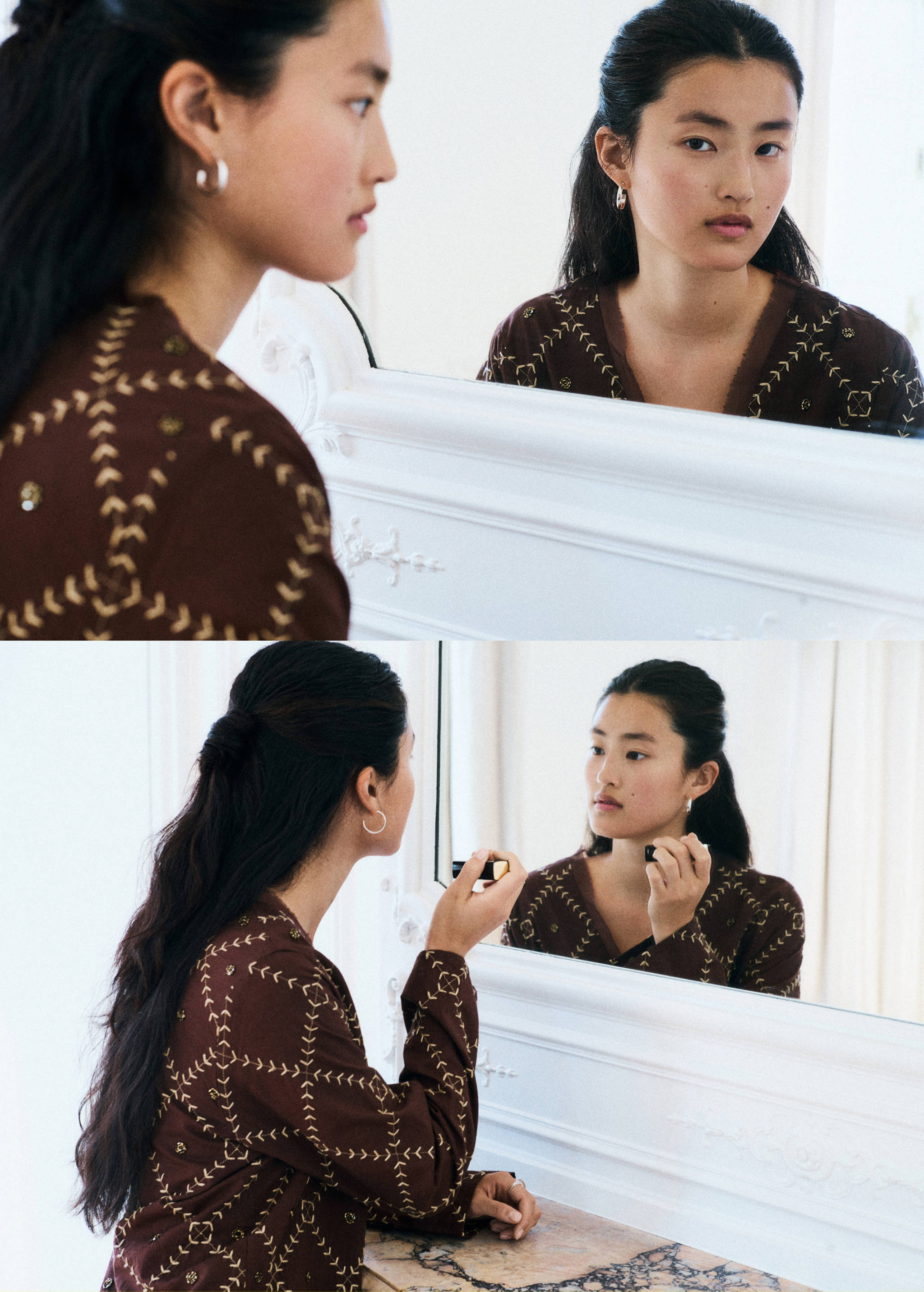 Close-up of a model wearing a brown embroidered top and silver hoop earrings, looking in a mirror.