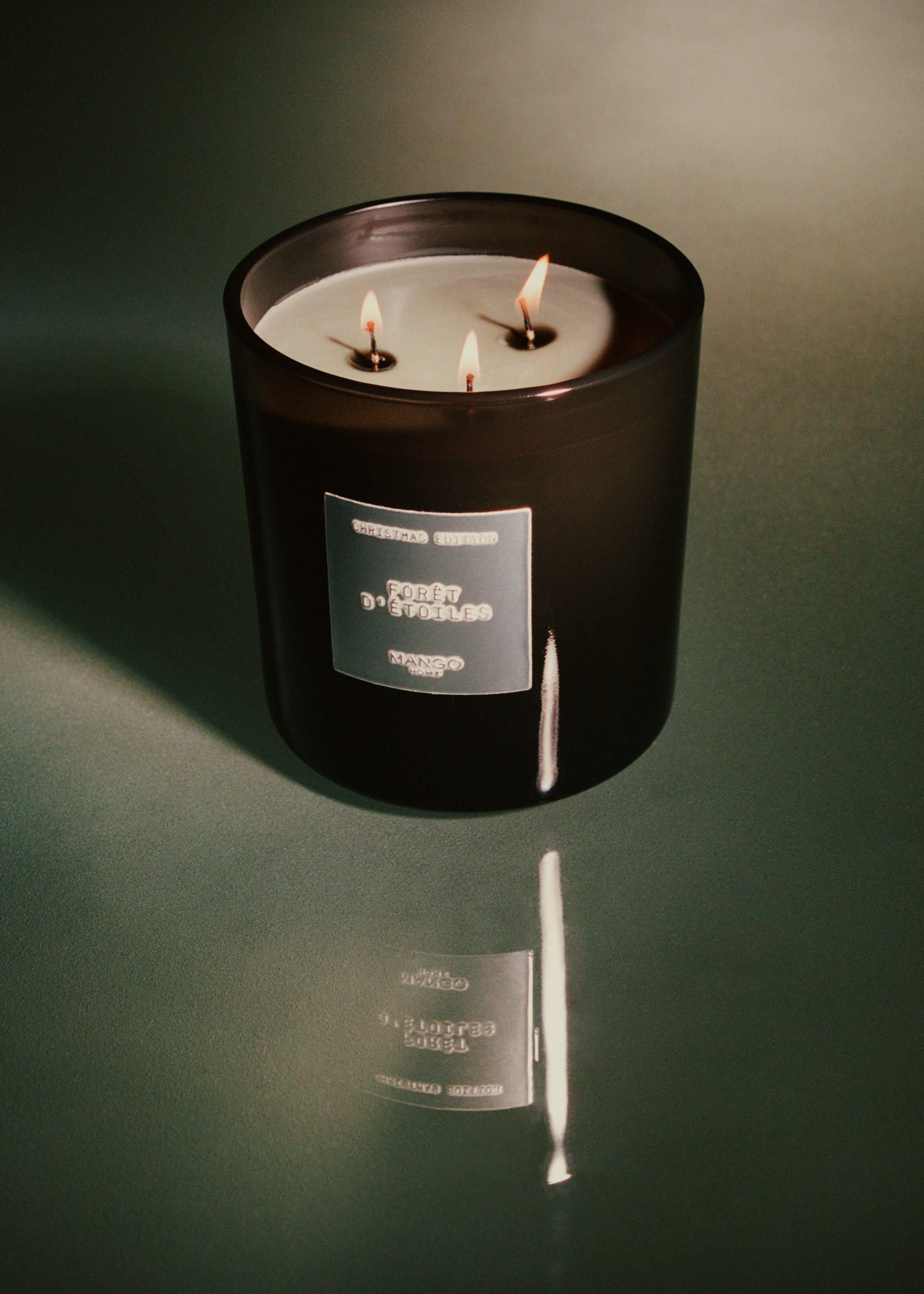 Dark glass jar candle with three lit wicks and a Christmas Edition label.