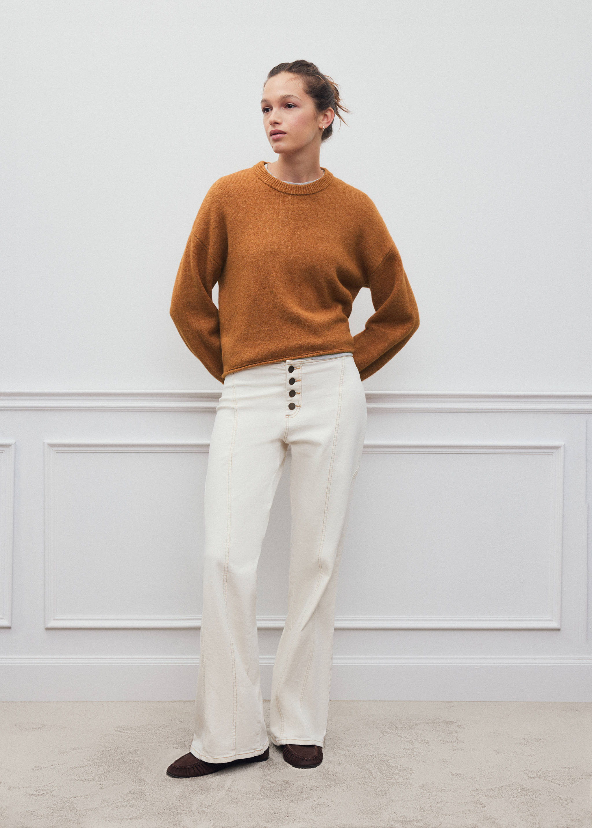 Jersey de punto en marrón óxido con cuello redondo y manga larga caída, combinado con pantalones acampanados en blanco roto.