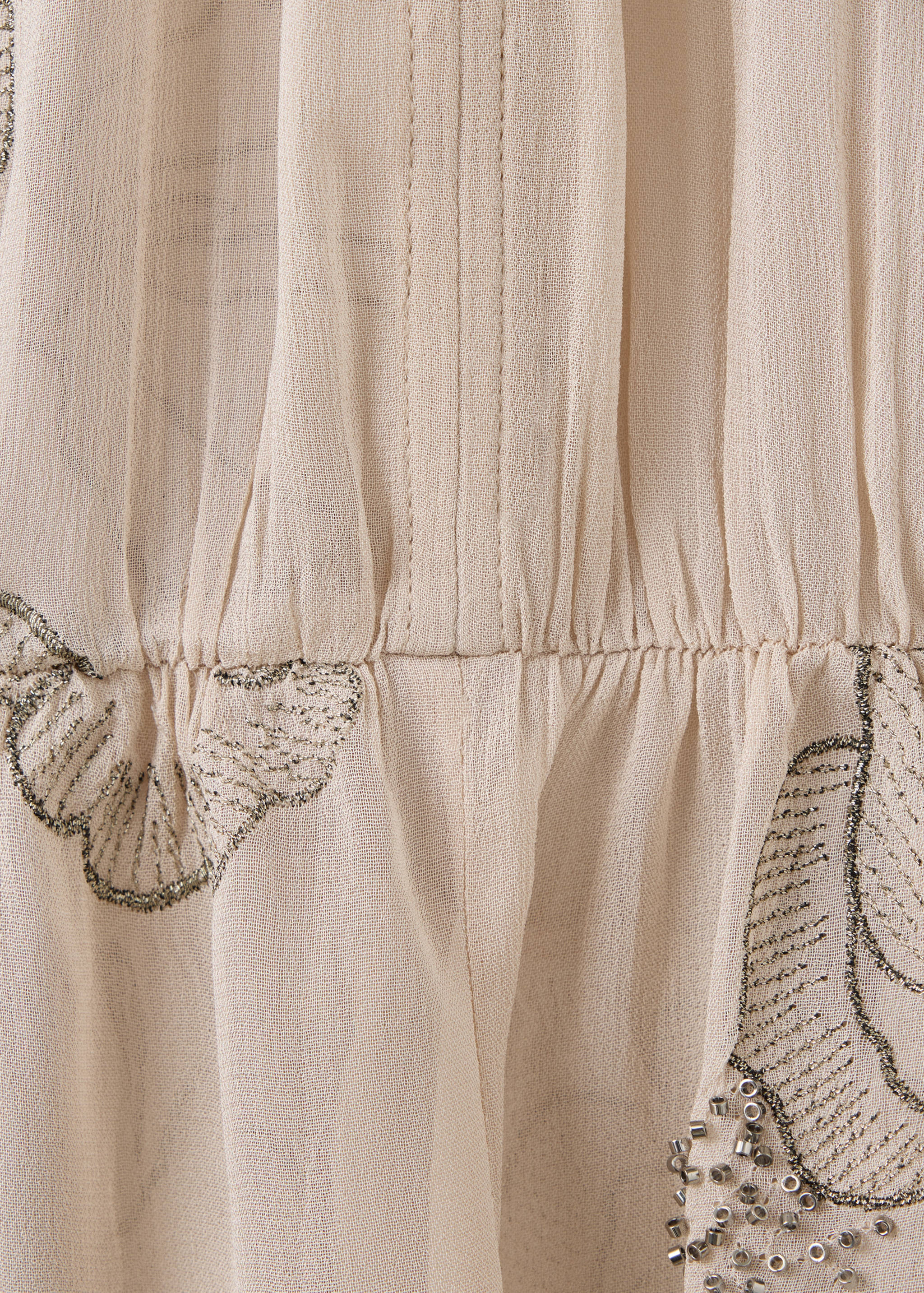 Primer plano del tejido de blusa en beige claro semitransparente con detalles de cuentas bordadas
