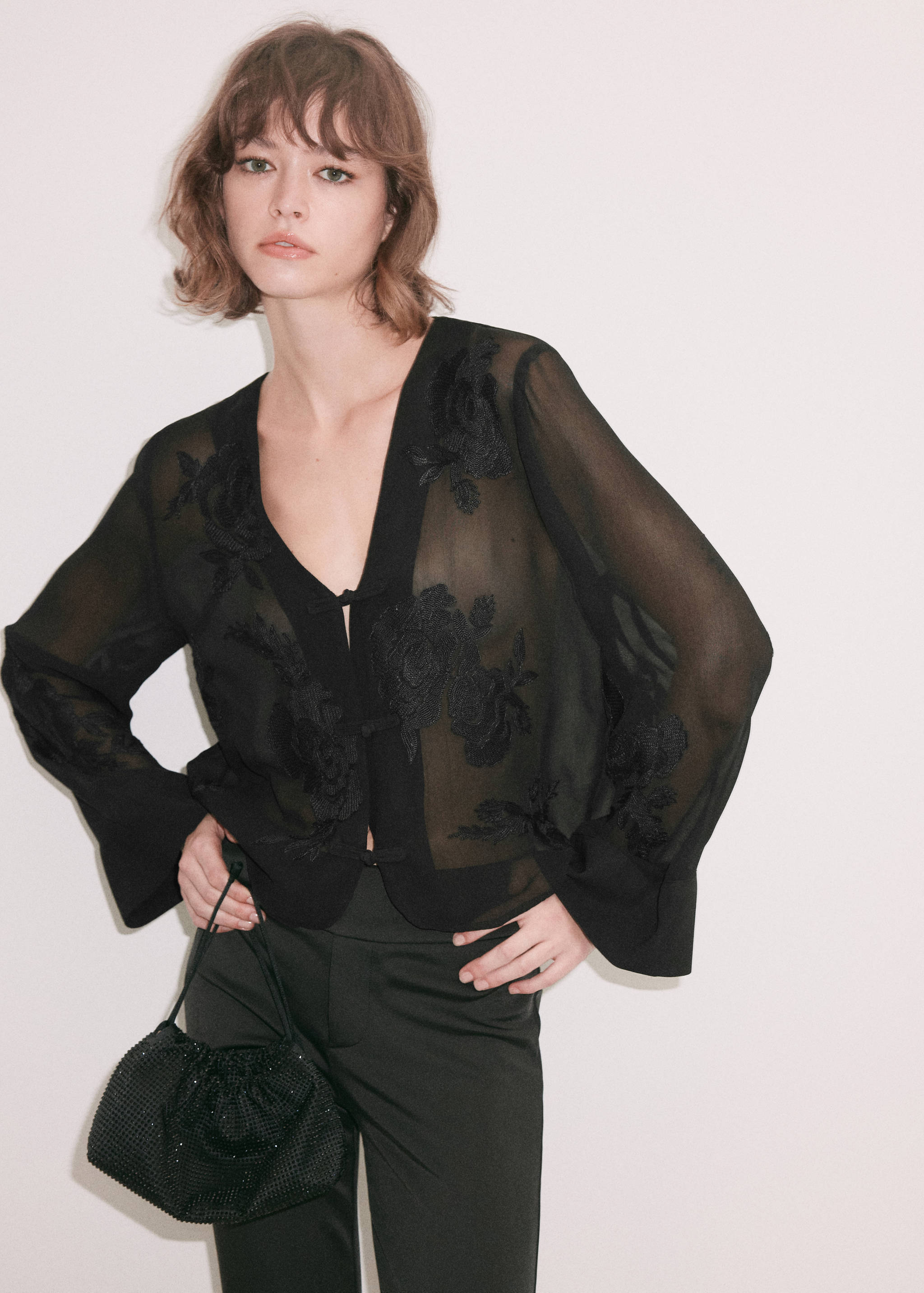 Blusa negra transparente con cuello en V, bordados florales al tono y manga larga.