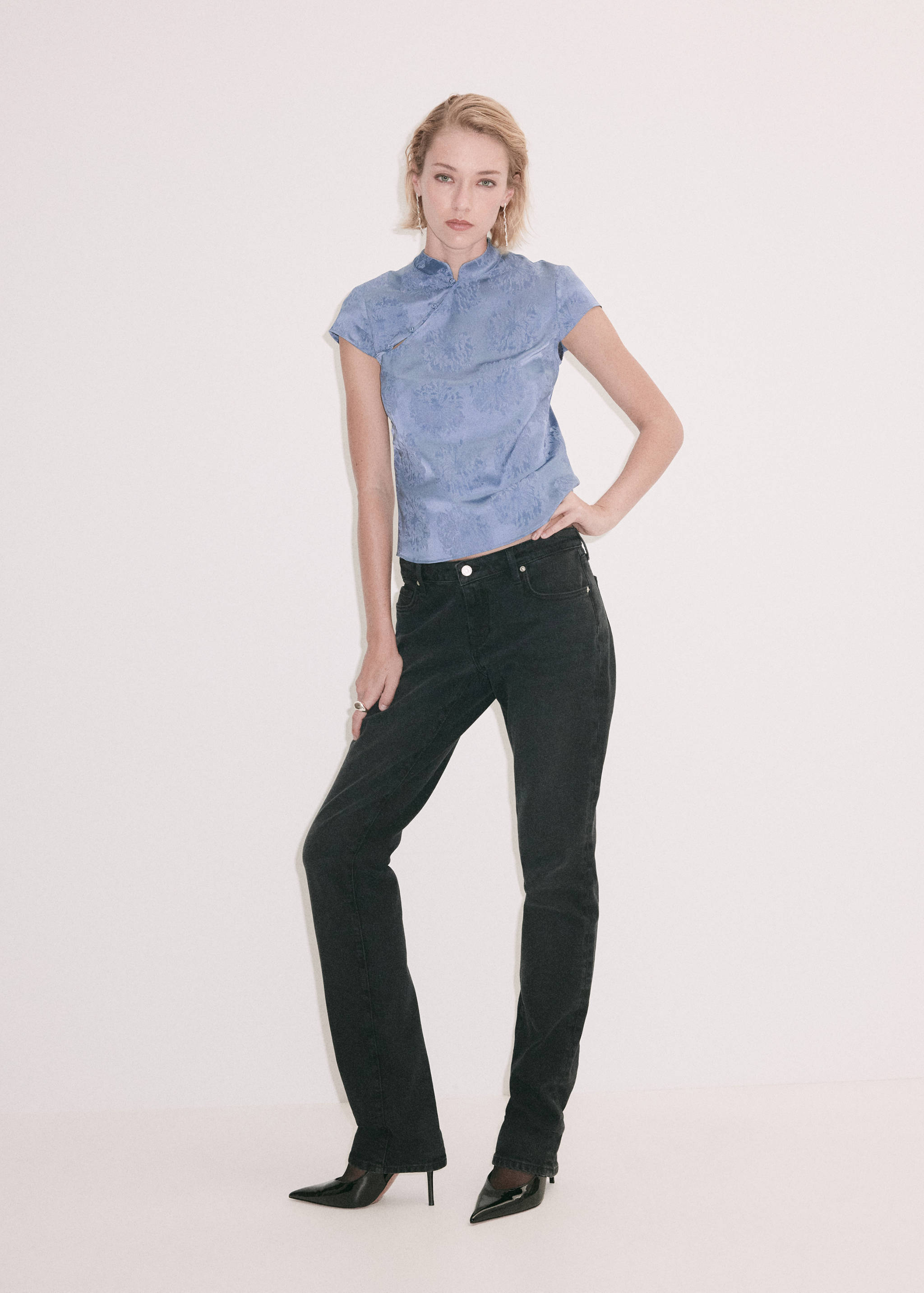 Blusa azul claro con estampado floral, cuello mao y manga sisa, combinada con pantalones negros.
