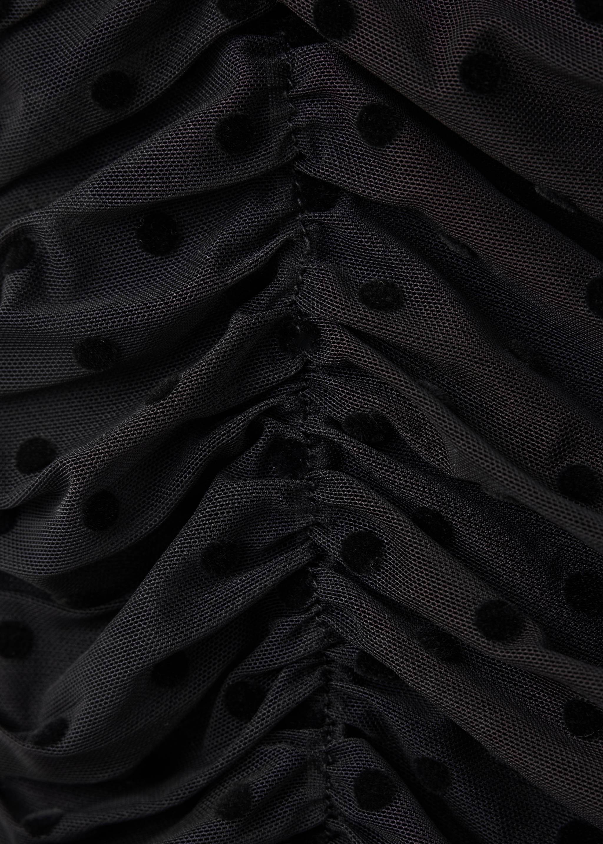 Close-up of a black mesh top with flocked dots and ruching.