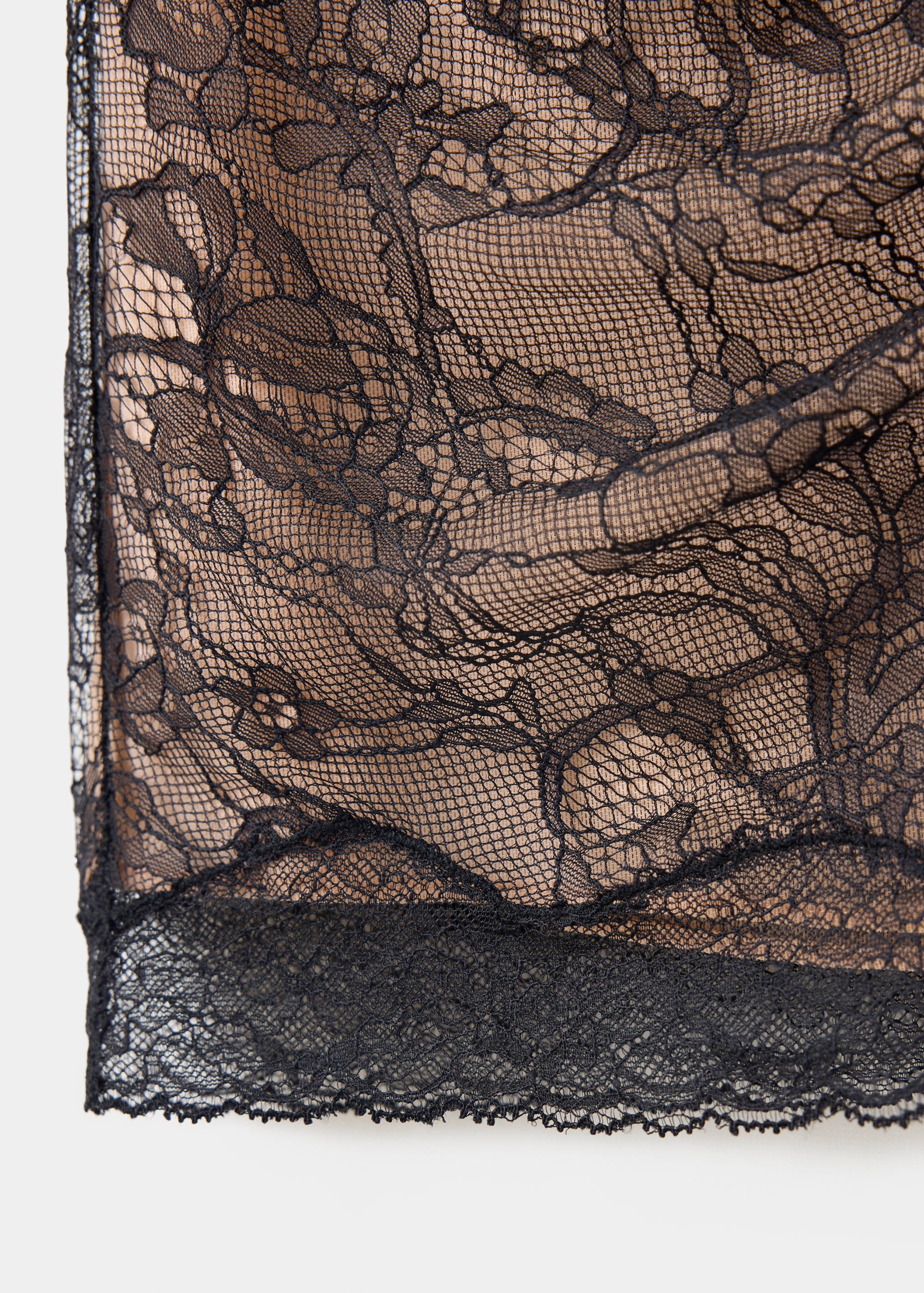 Close-up of a black lace skirt fabric with floral pattern and nude lining.