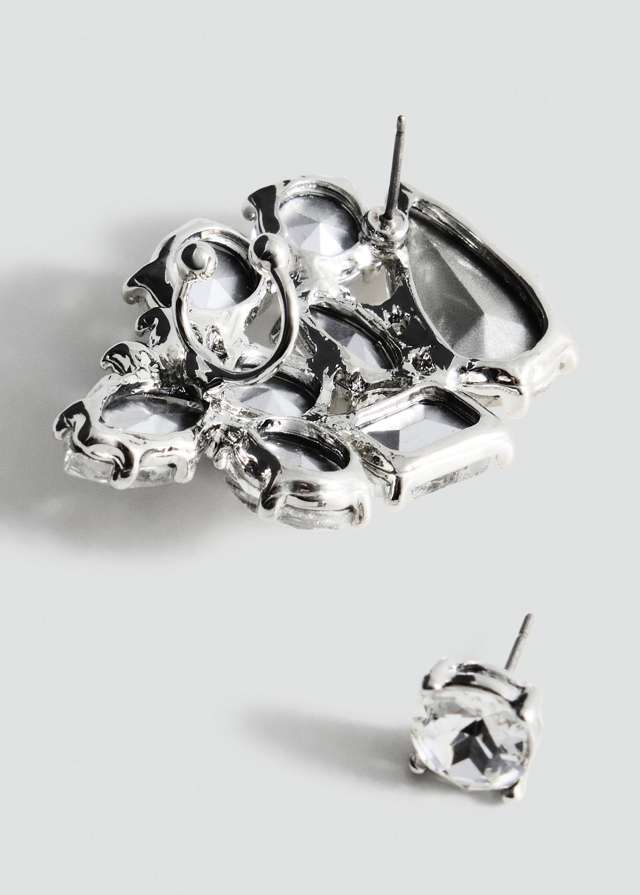 Close-up of silver-tone stud earrings with faceted clear stones.