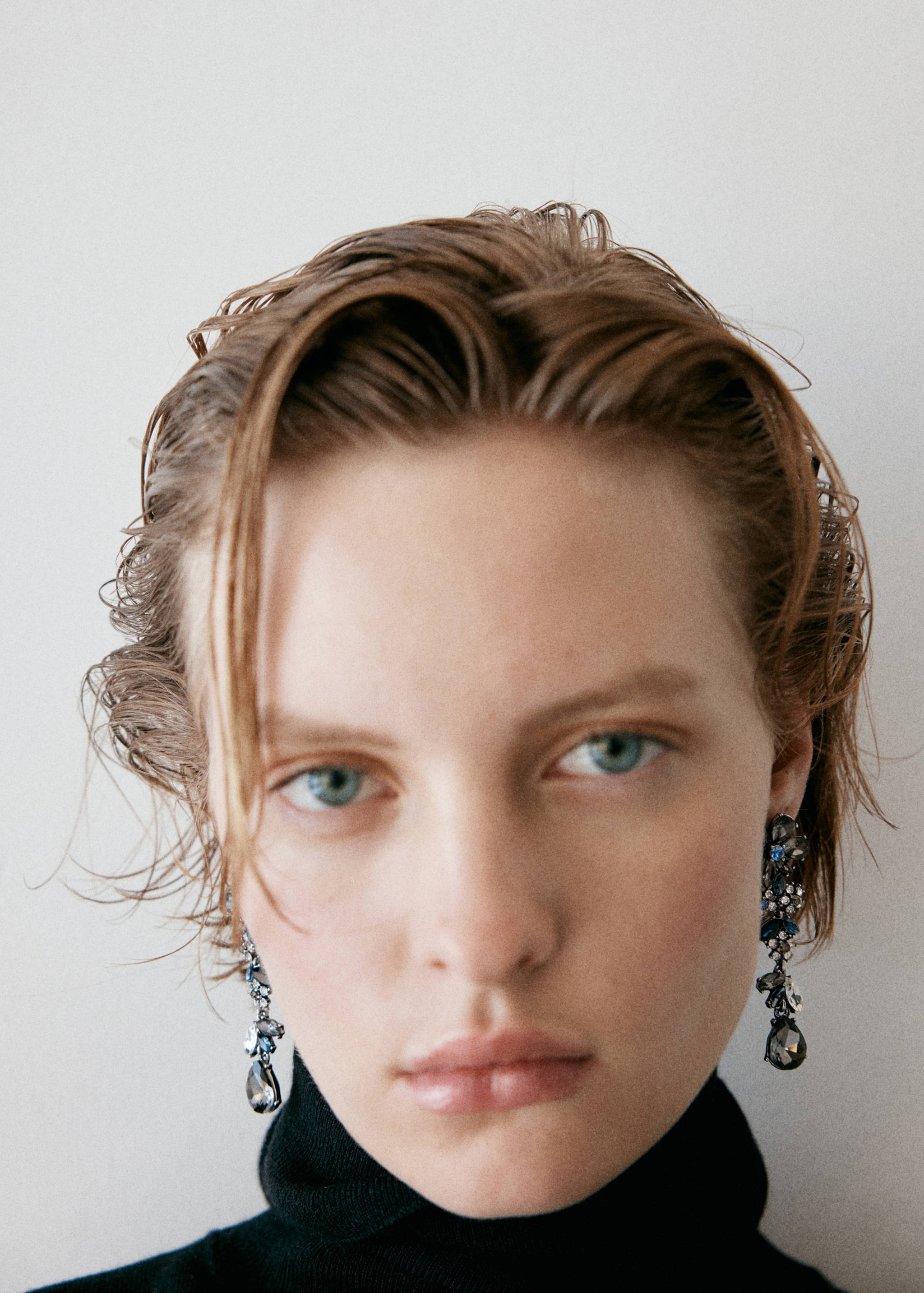 Hanging earrings with blue and dark crystals on a model.