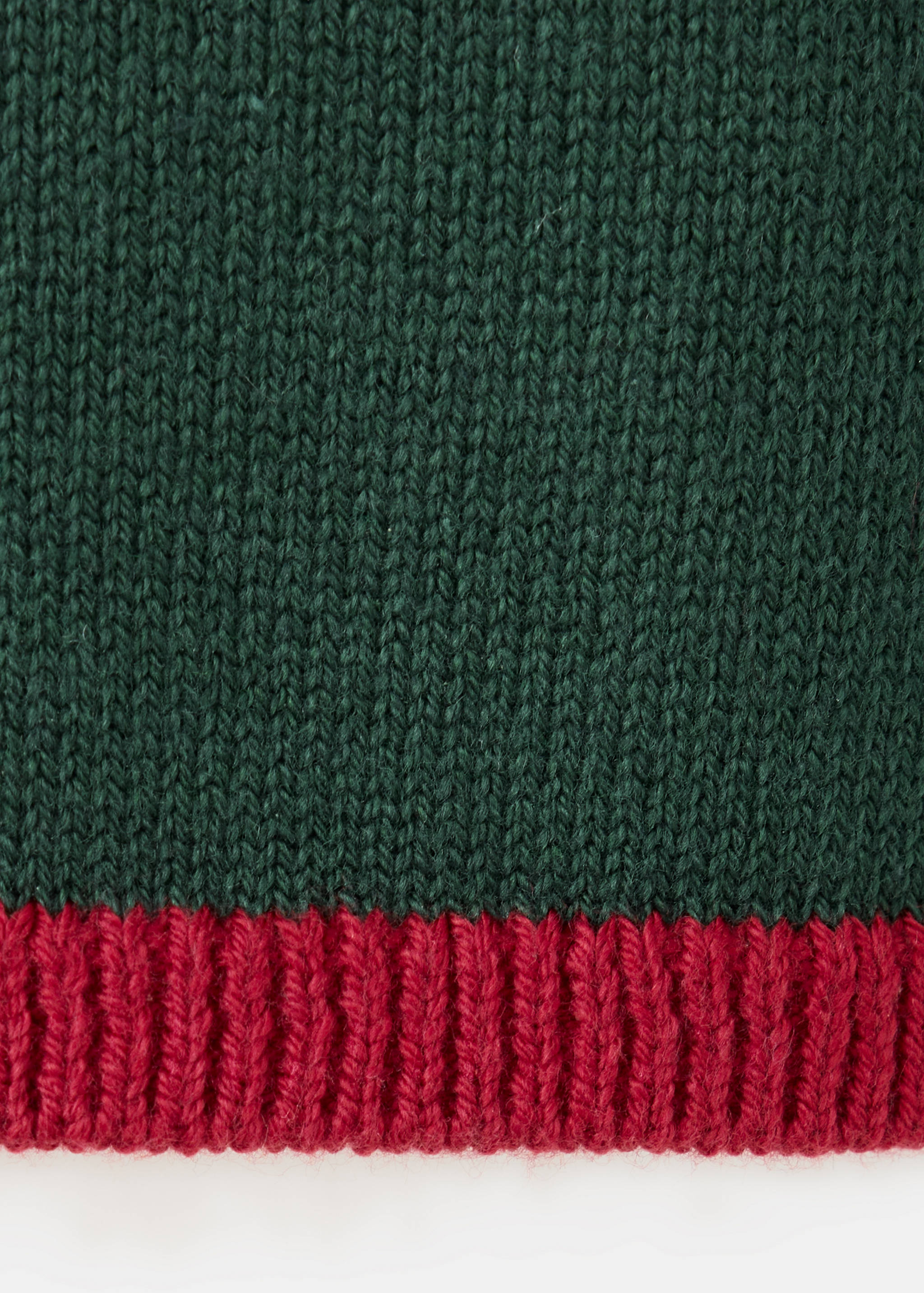 Close-up of a dark green knit jumper with a red ribbed hem.