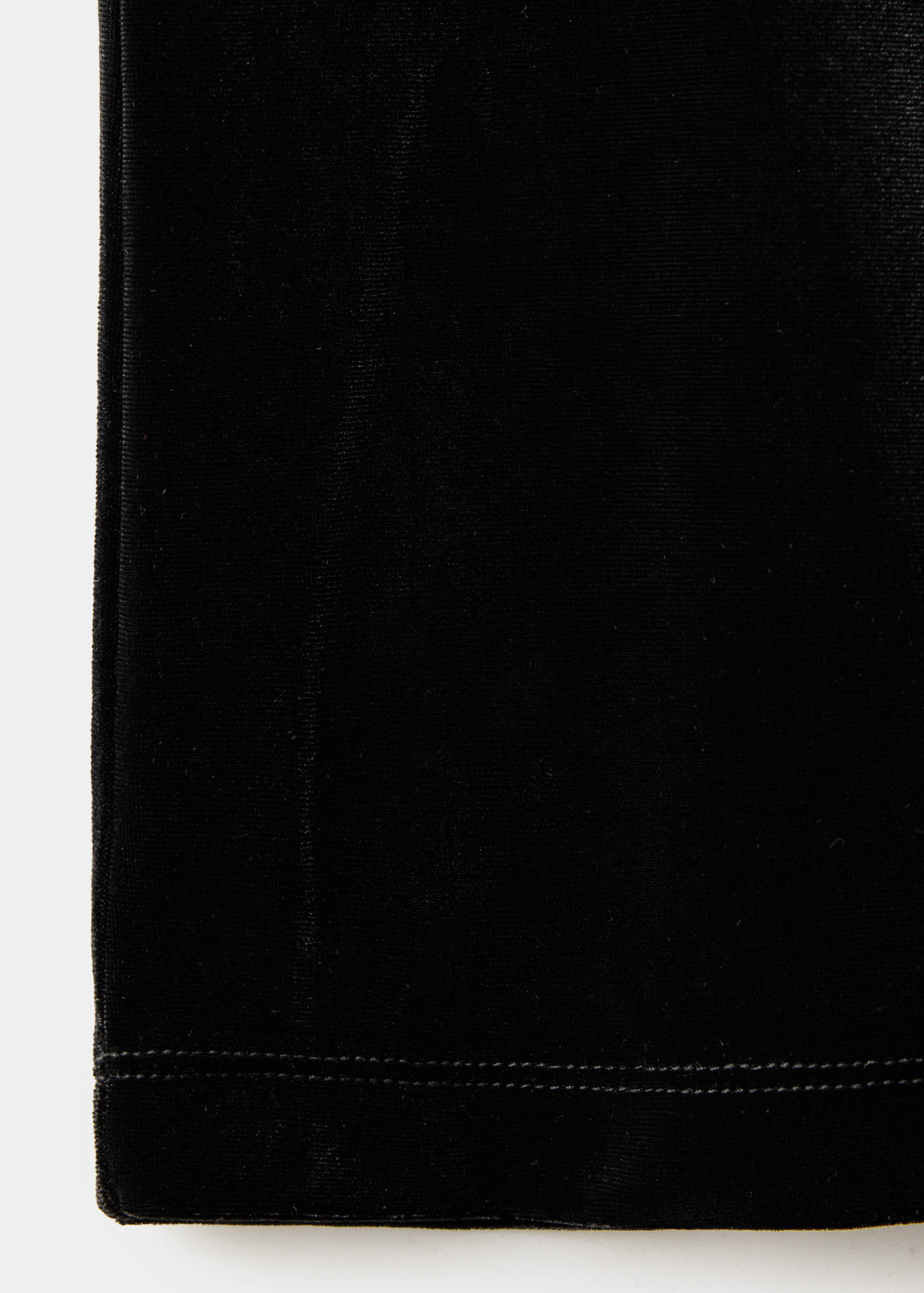 Close-up of black velvet trousers fabric detail showing texture and hem stitching.
