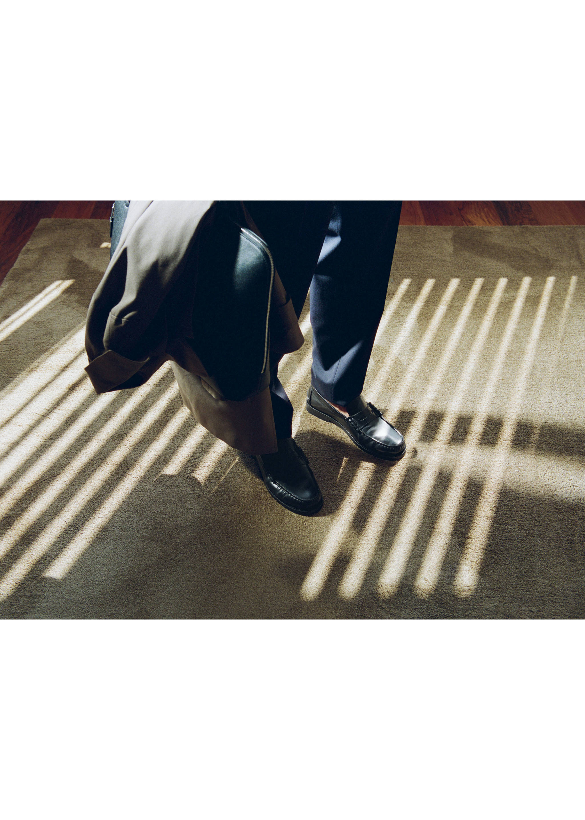 Black leather penny loafers worn with dark trousers on a carpet., Black. Ref: 37021465-00.