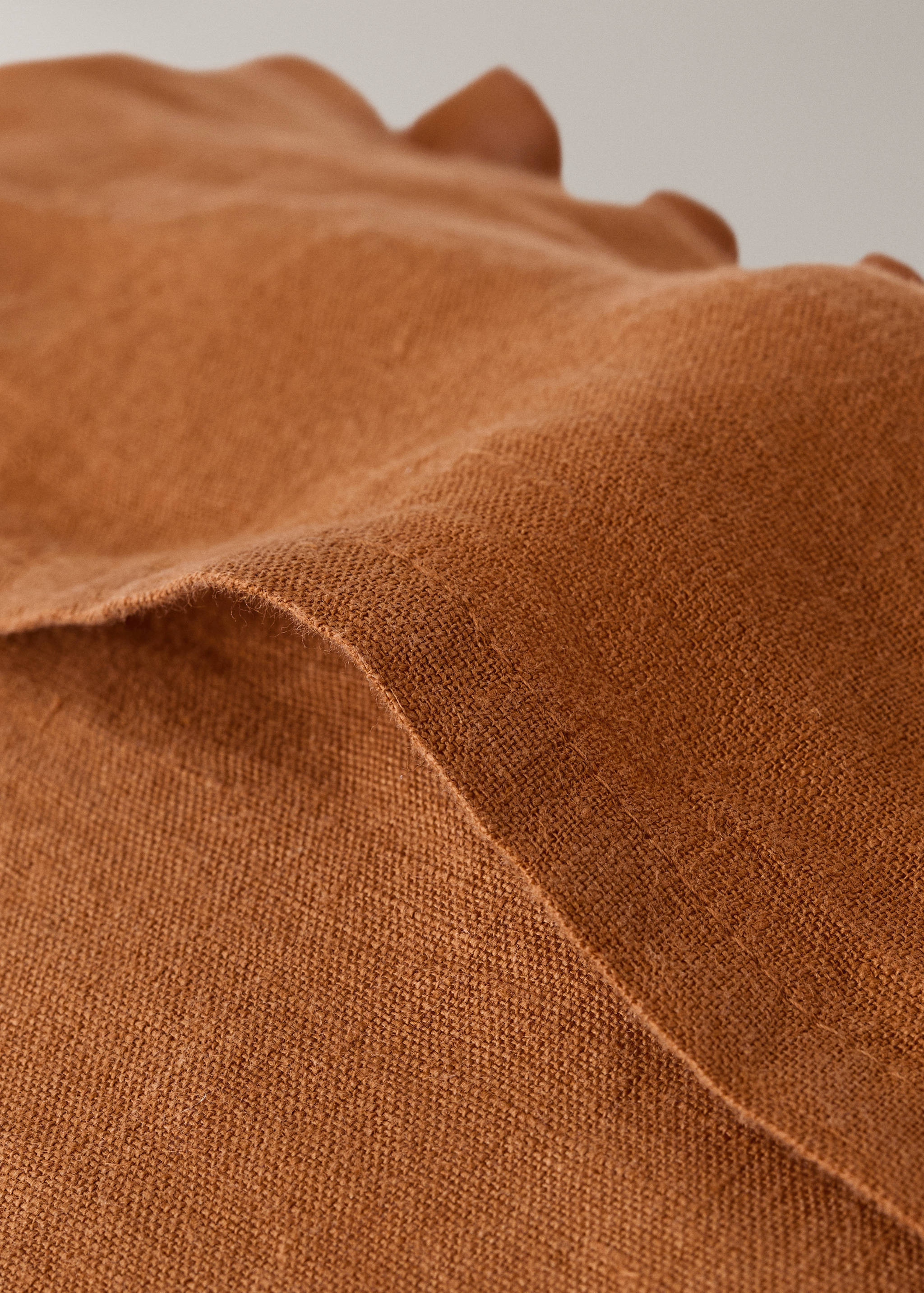 Brown cushion cover detail showing textured fabric and ruffled edge.