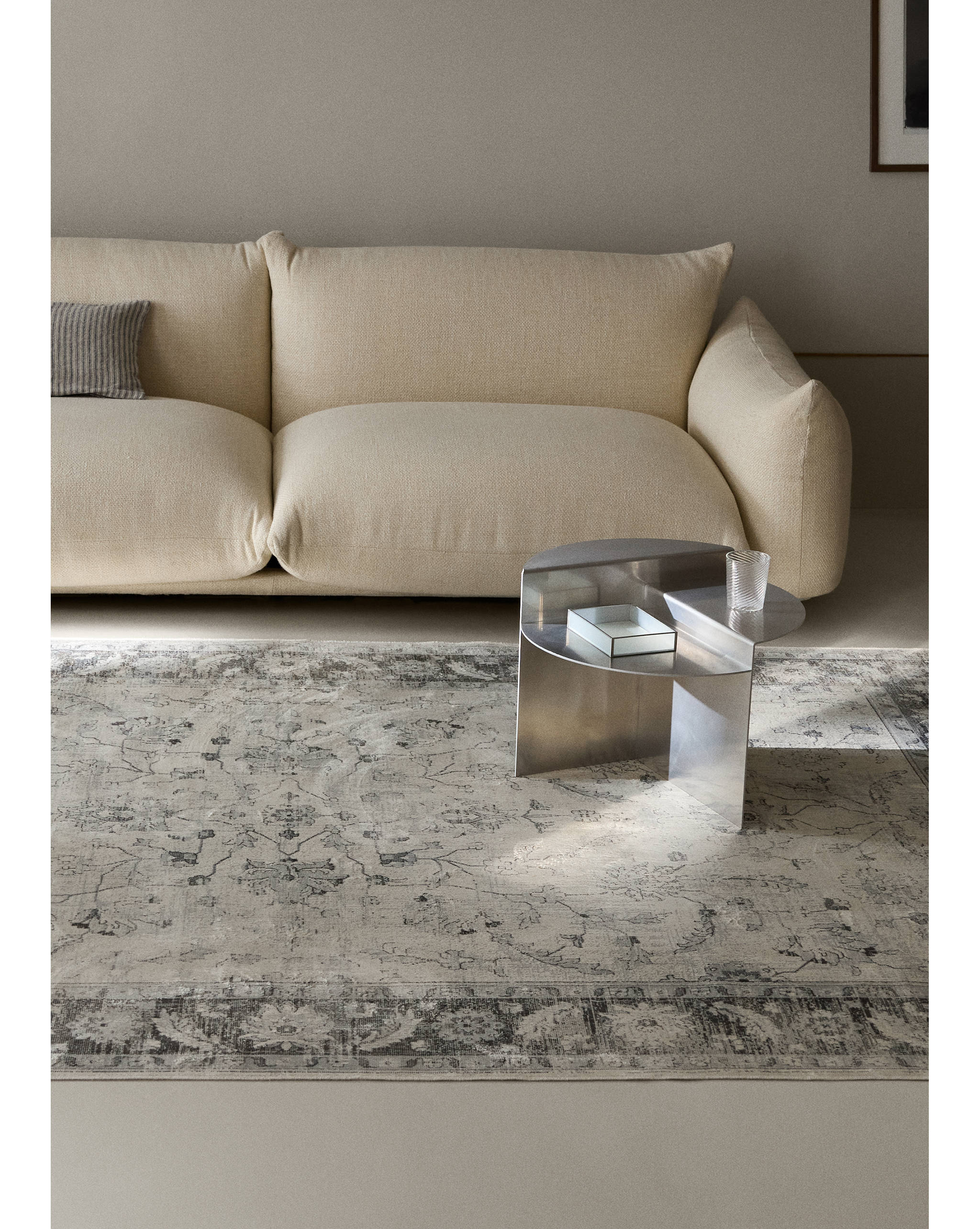 Beige rug with a dark grey ornate floral pattern in a living room setting.