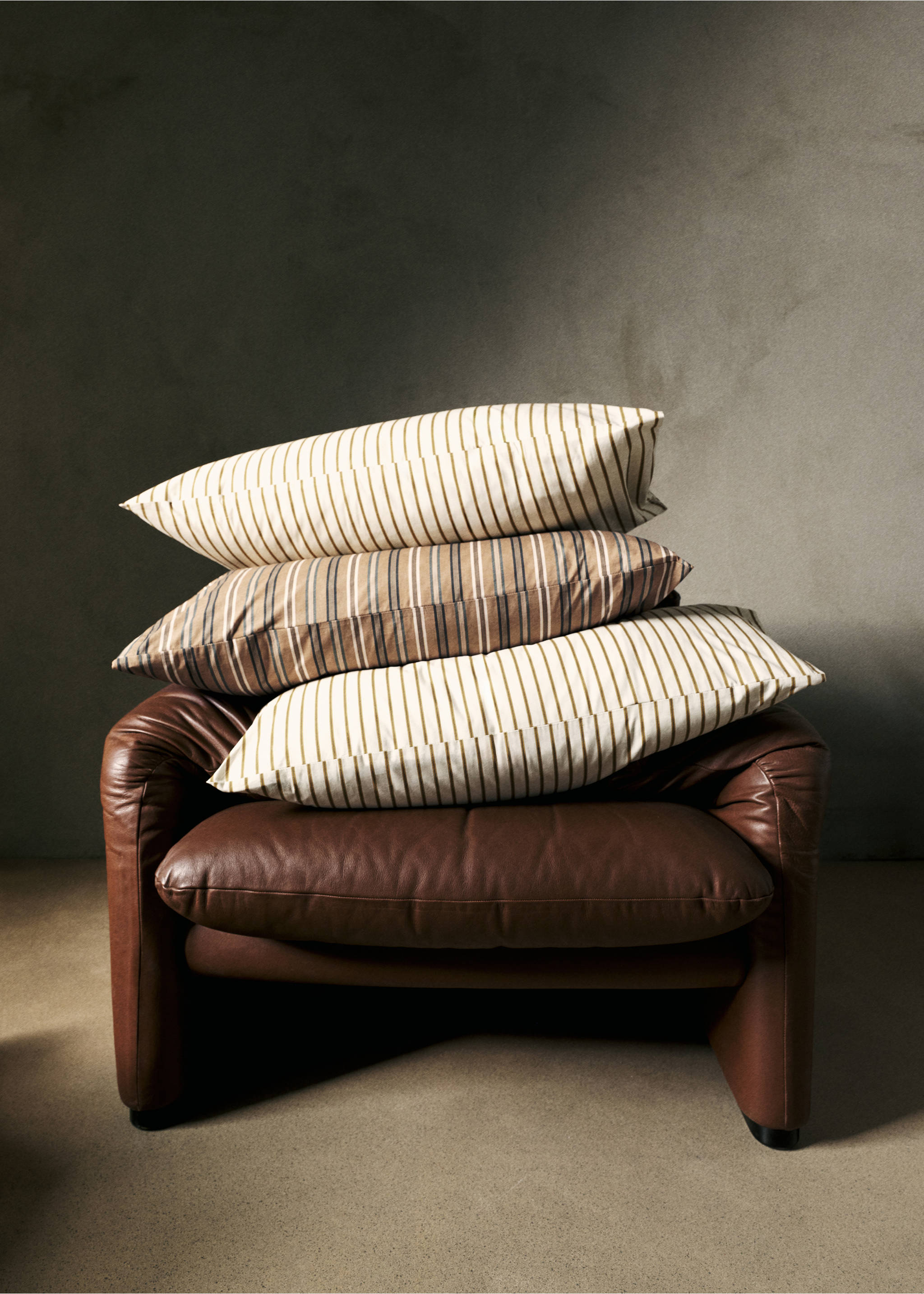 Striped pillowcases stacked on a brown leather armchair., Tobacco Brown. Ref: 37022954-00.