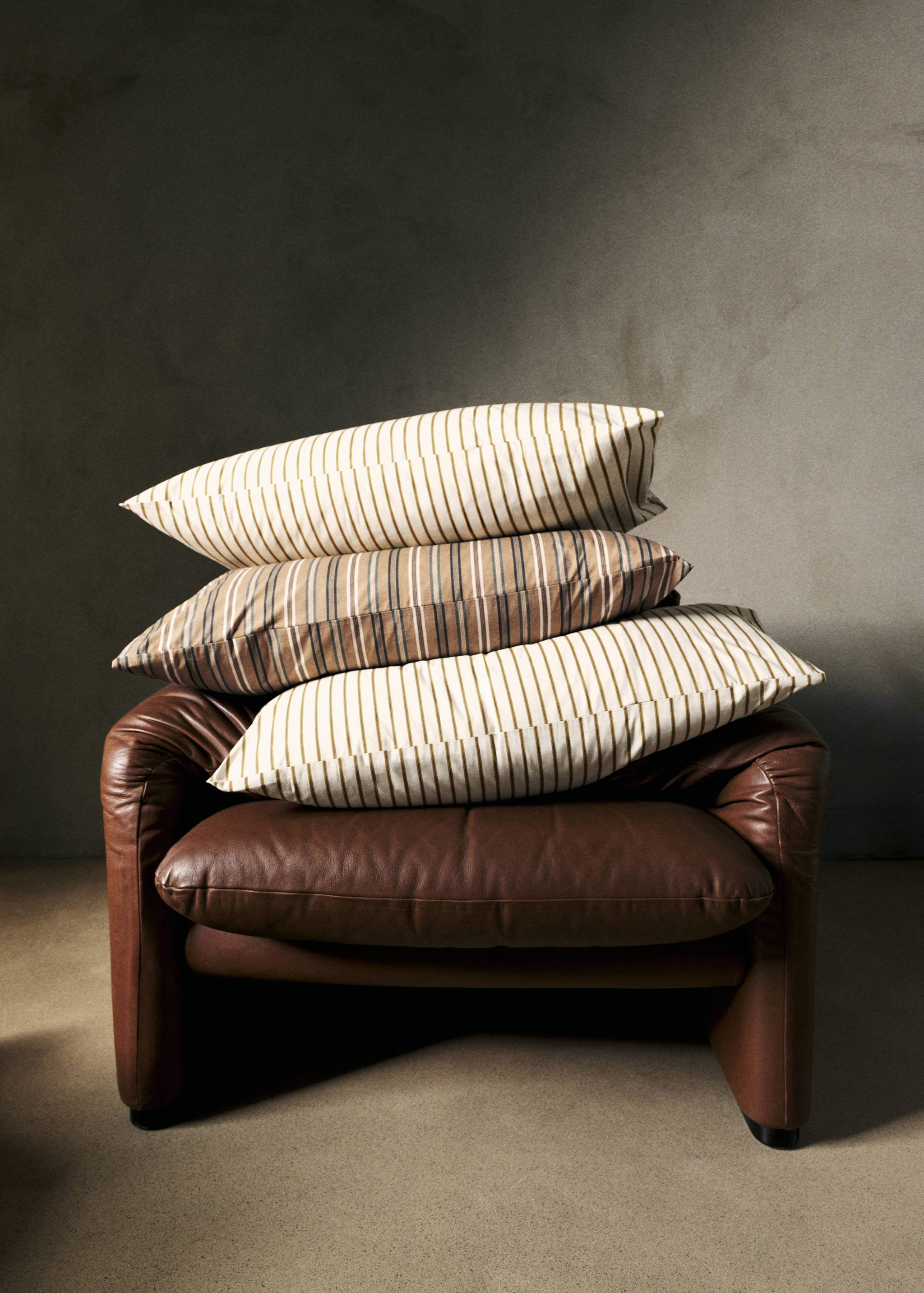 Striped pillowcases stacked on a brown leather armchair.
