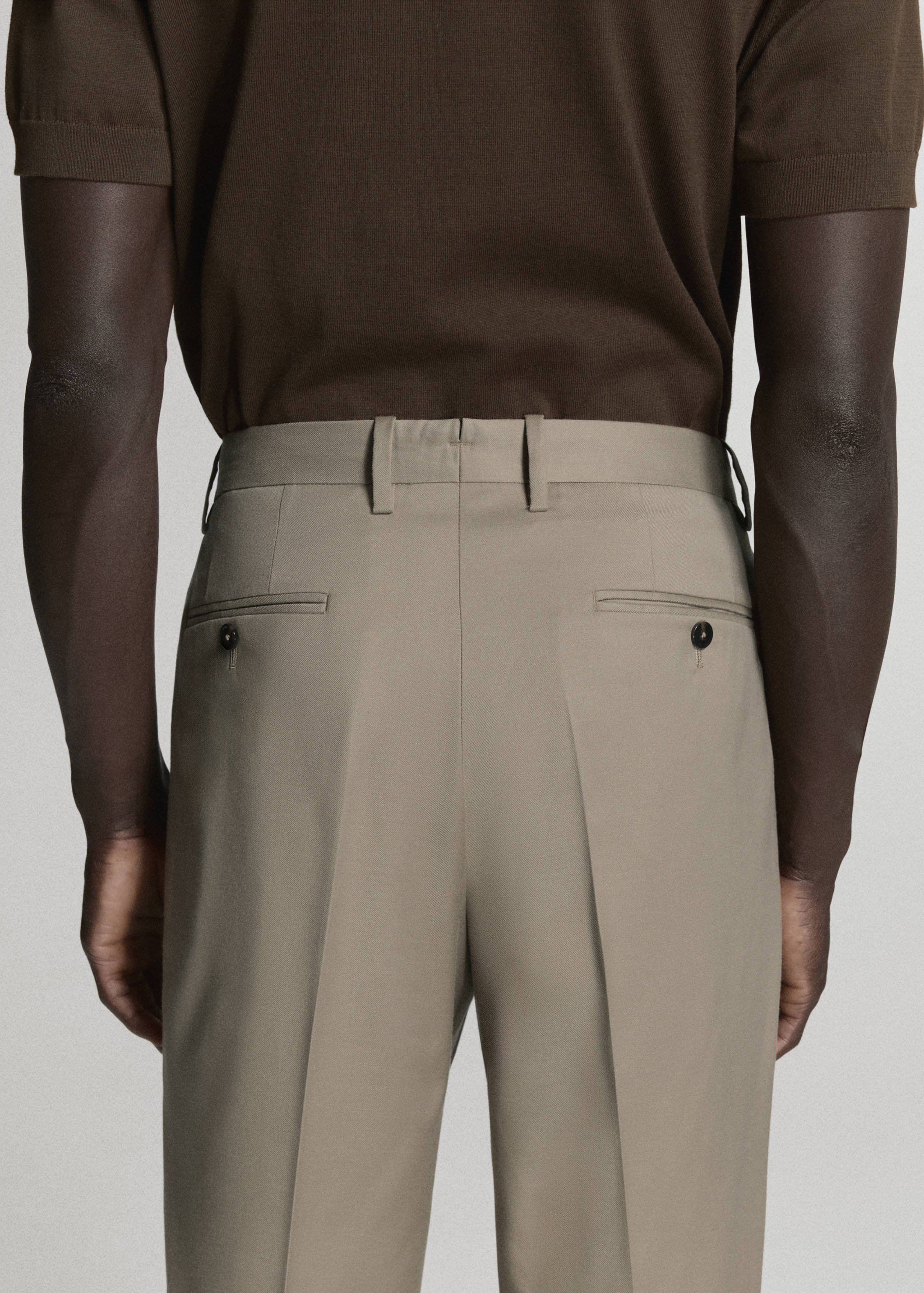 Beige trousers featuring back buttoned pockets, seen from behind.
