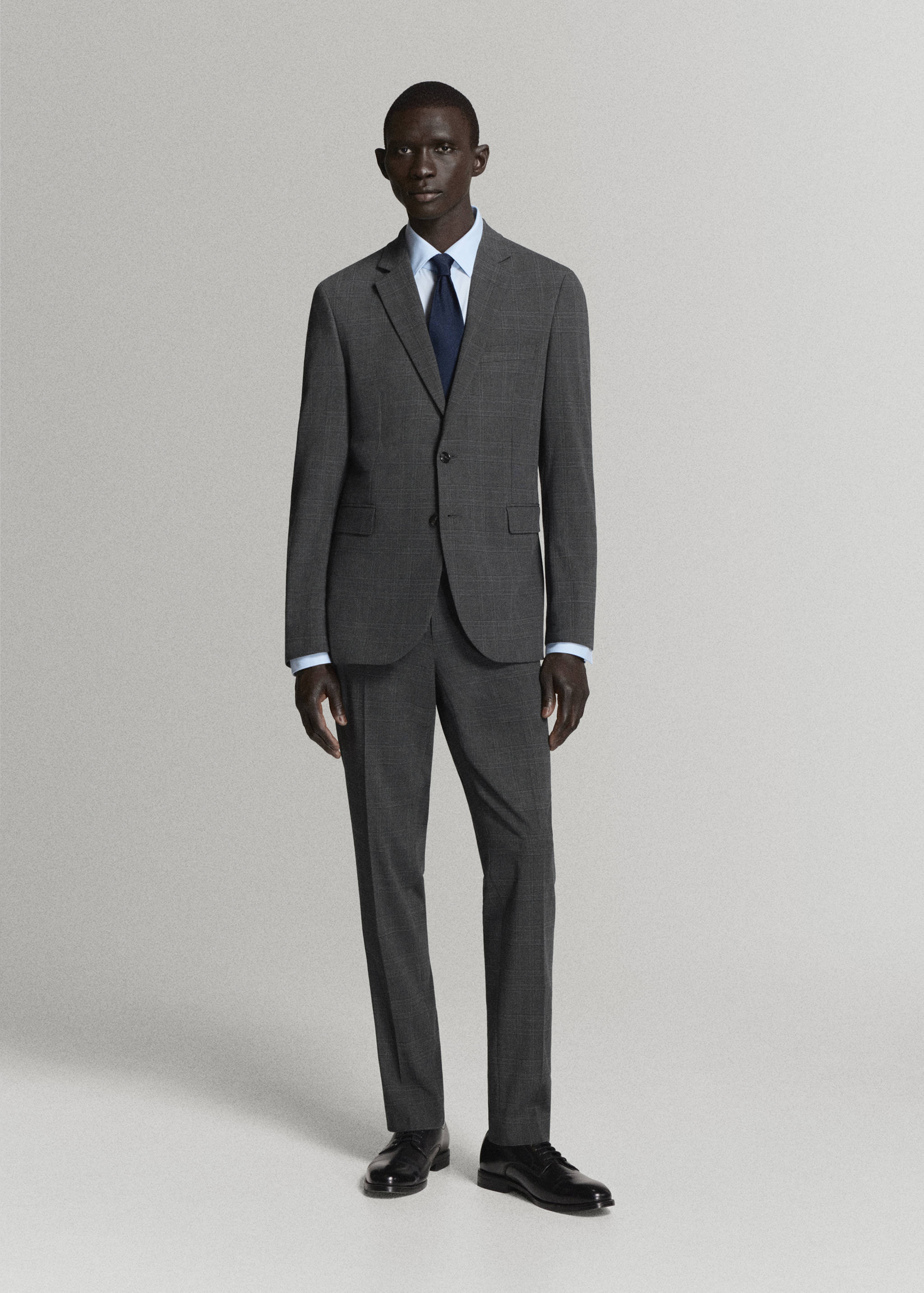Dark grey tailored suit trousers worn with a matching suit jacket, light blue shirt, and dark tie.
