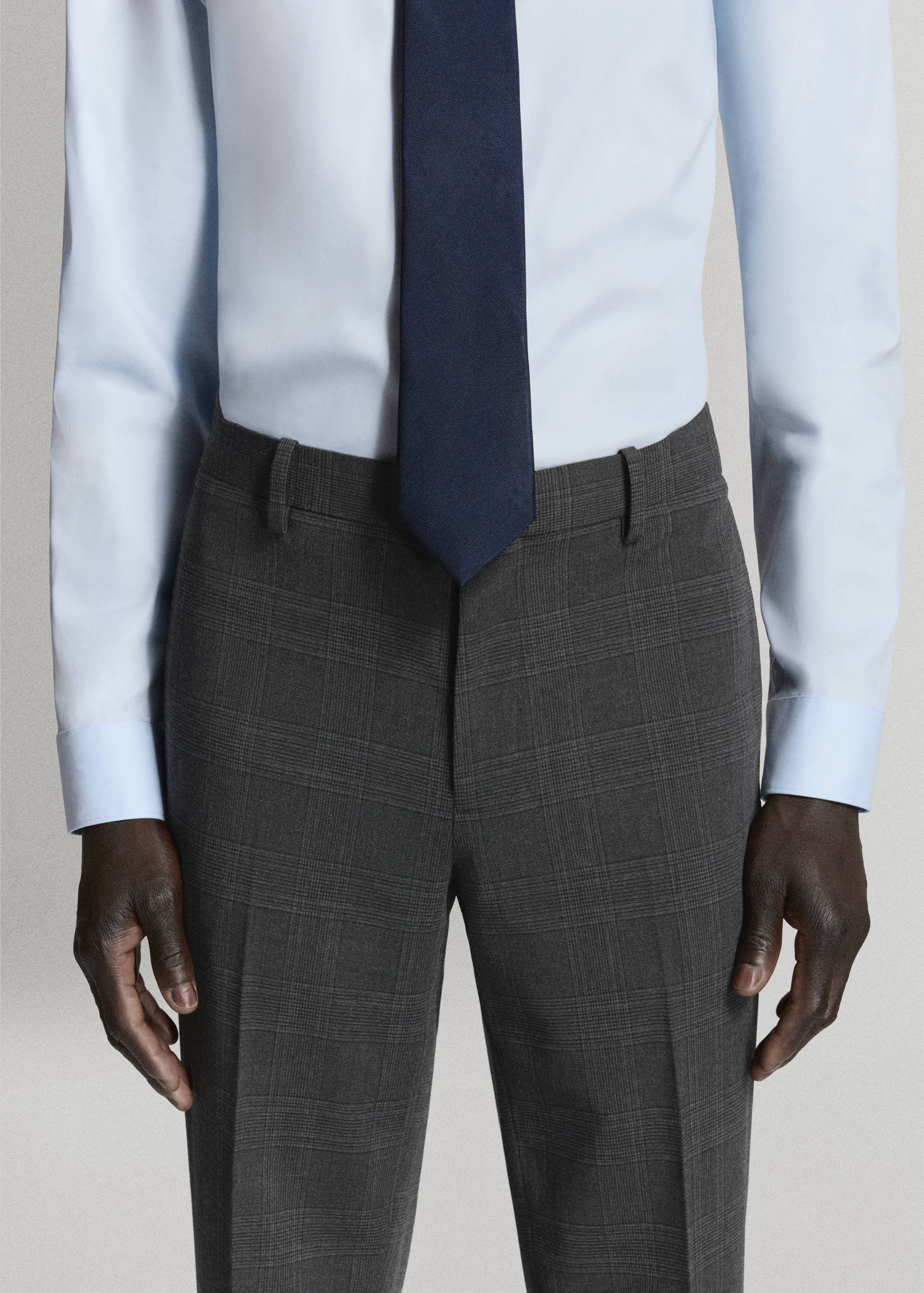 Dark grey checked trousers styled with a light blue shirt and a navy tie.
