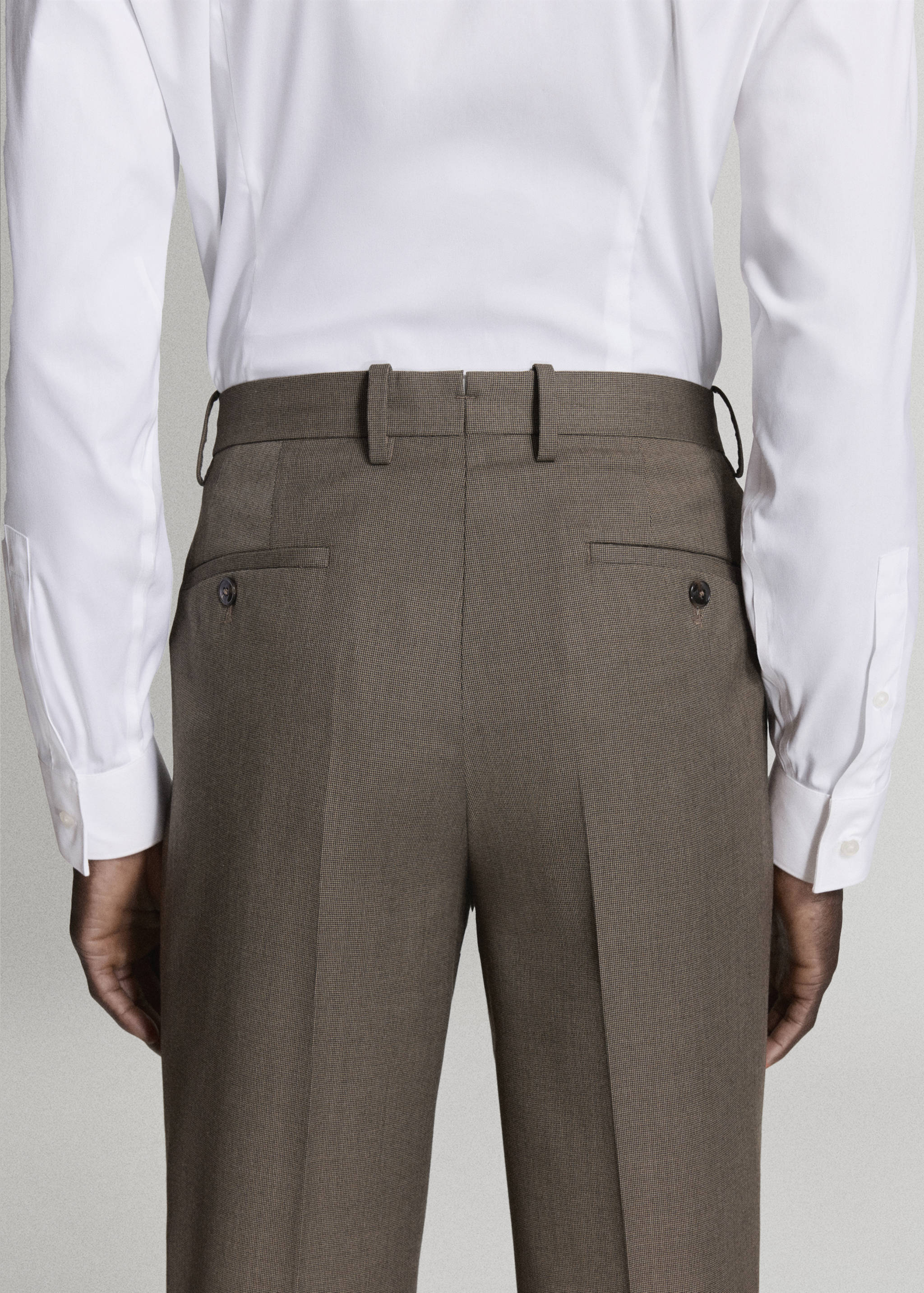 Brown trousers viewed from the back, paired with a white shirt.