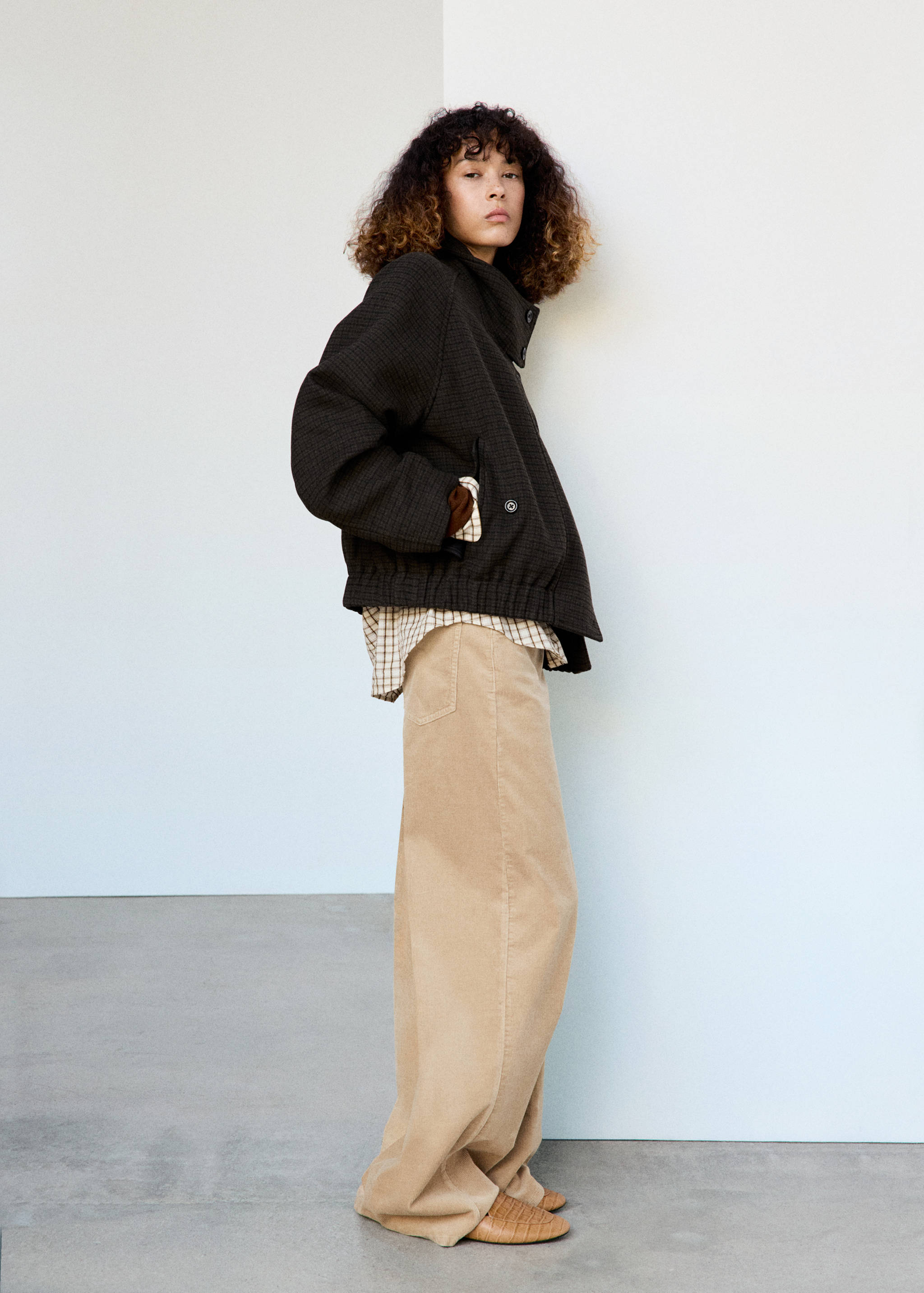Dark brown textured jacket with a high collar and elasticated hem, worn with a checked shirt and beige trousers.