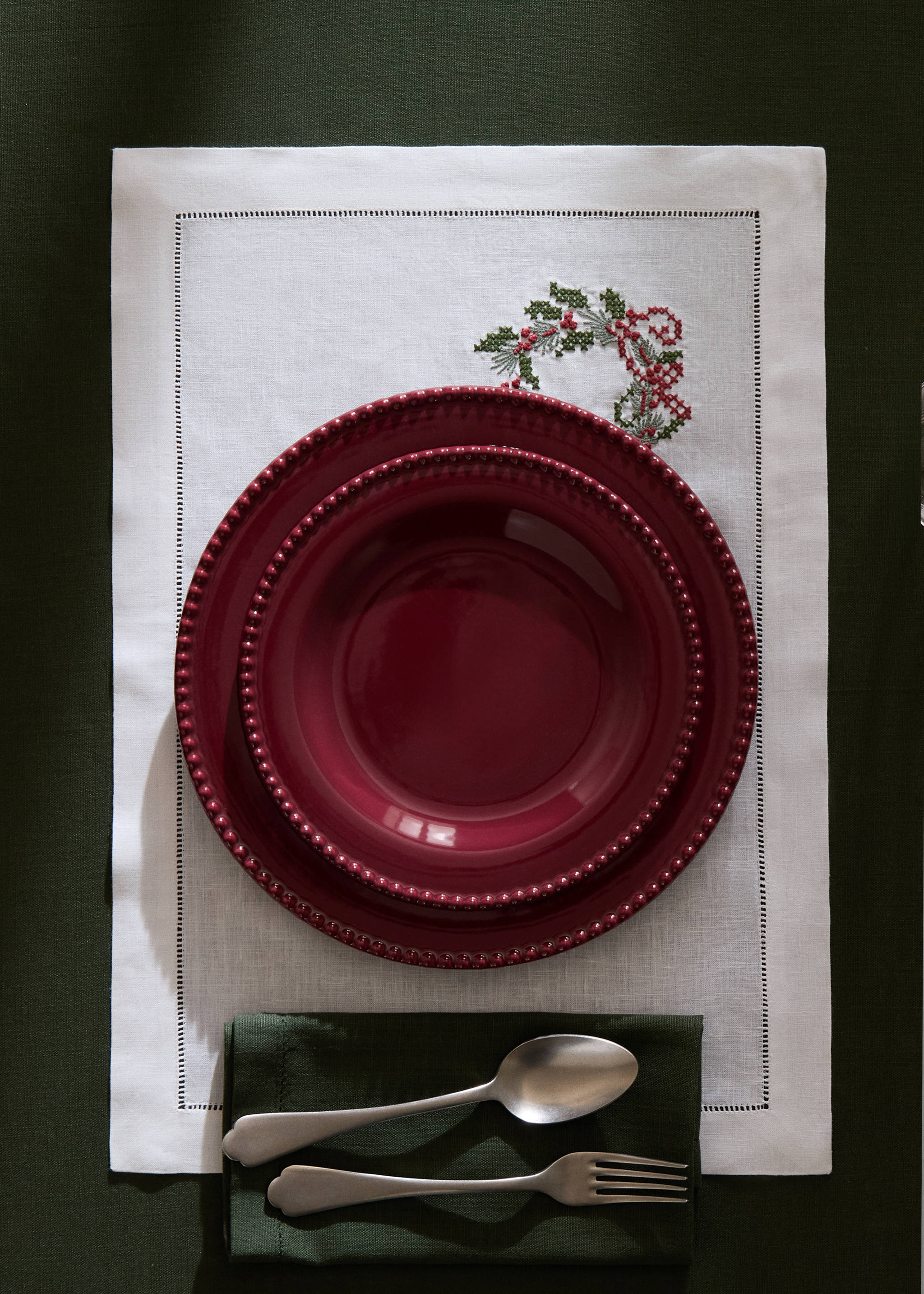 White embroidered Christmas placemat with red and green festive details, set with red plates and cutlery., White. Ref: 37026334-00.