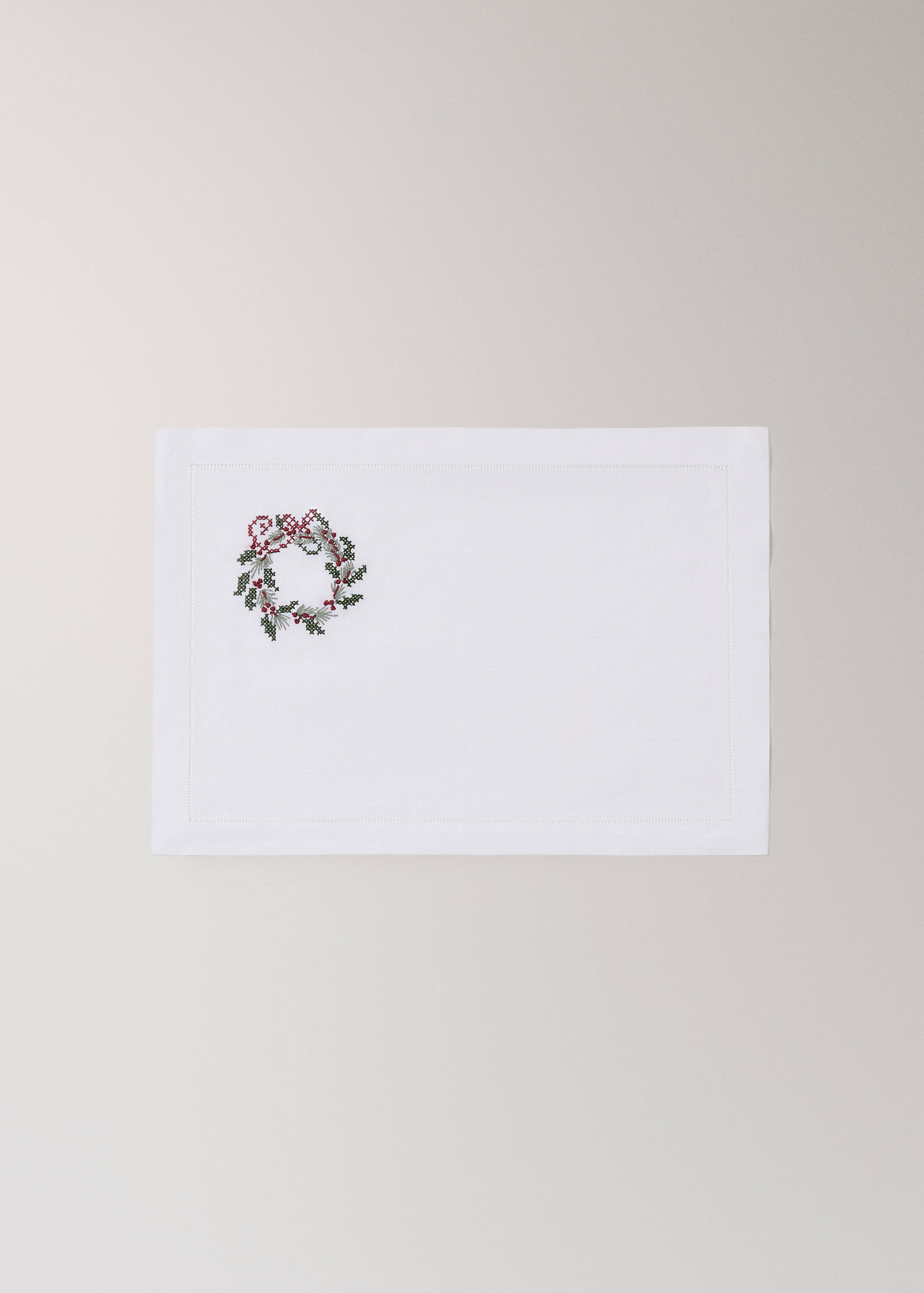 White placemat with an embroidered Christmas wreath motif.