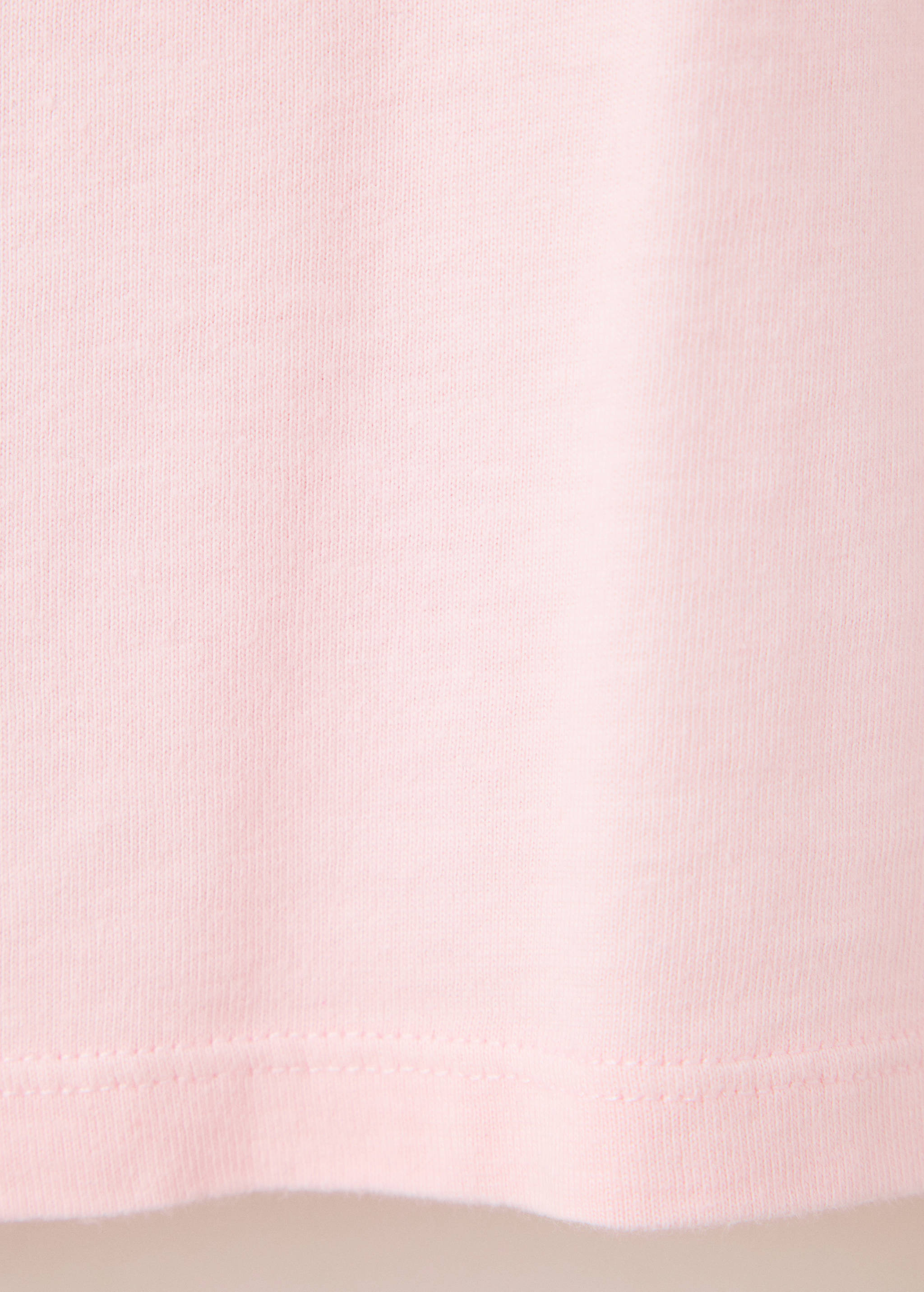 Close-up of the light pink fabric and hem of a t-shirt.