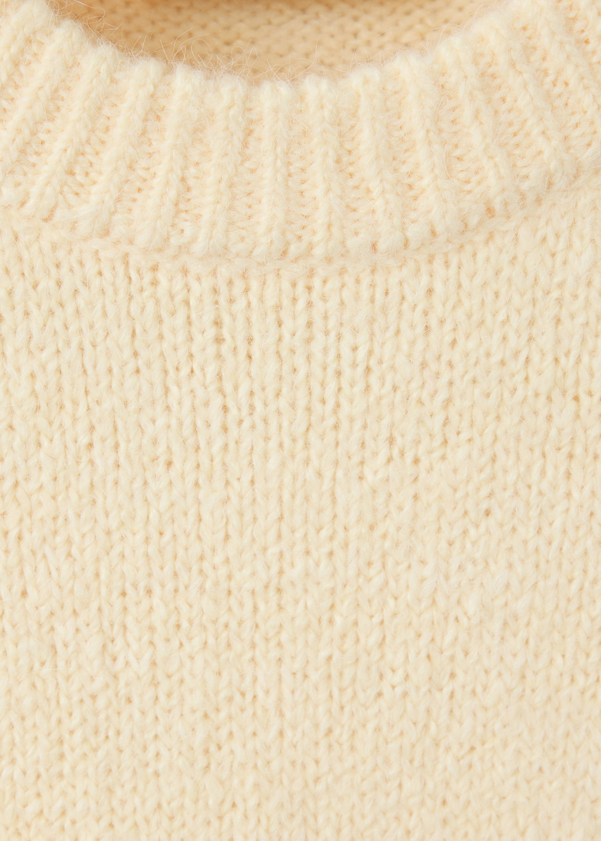 Cream sweater detail showing the ribbed neckline and knit texture.