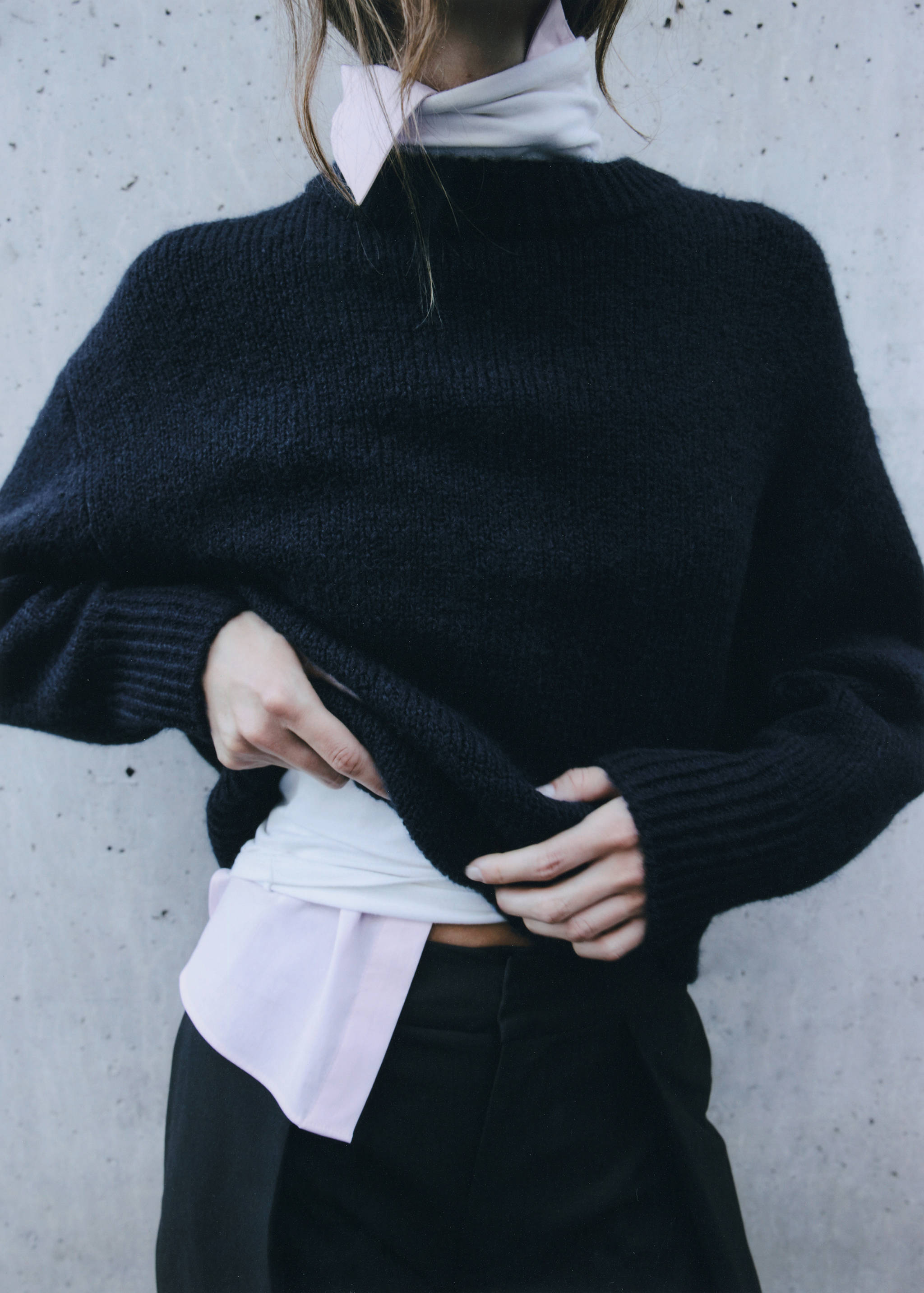 Black knit crew neck sweater layered over a collared shirt.