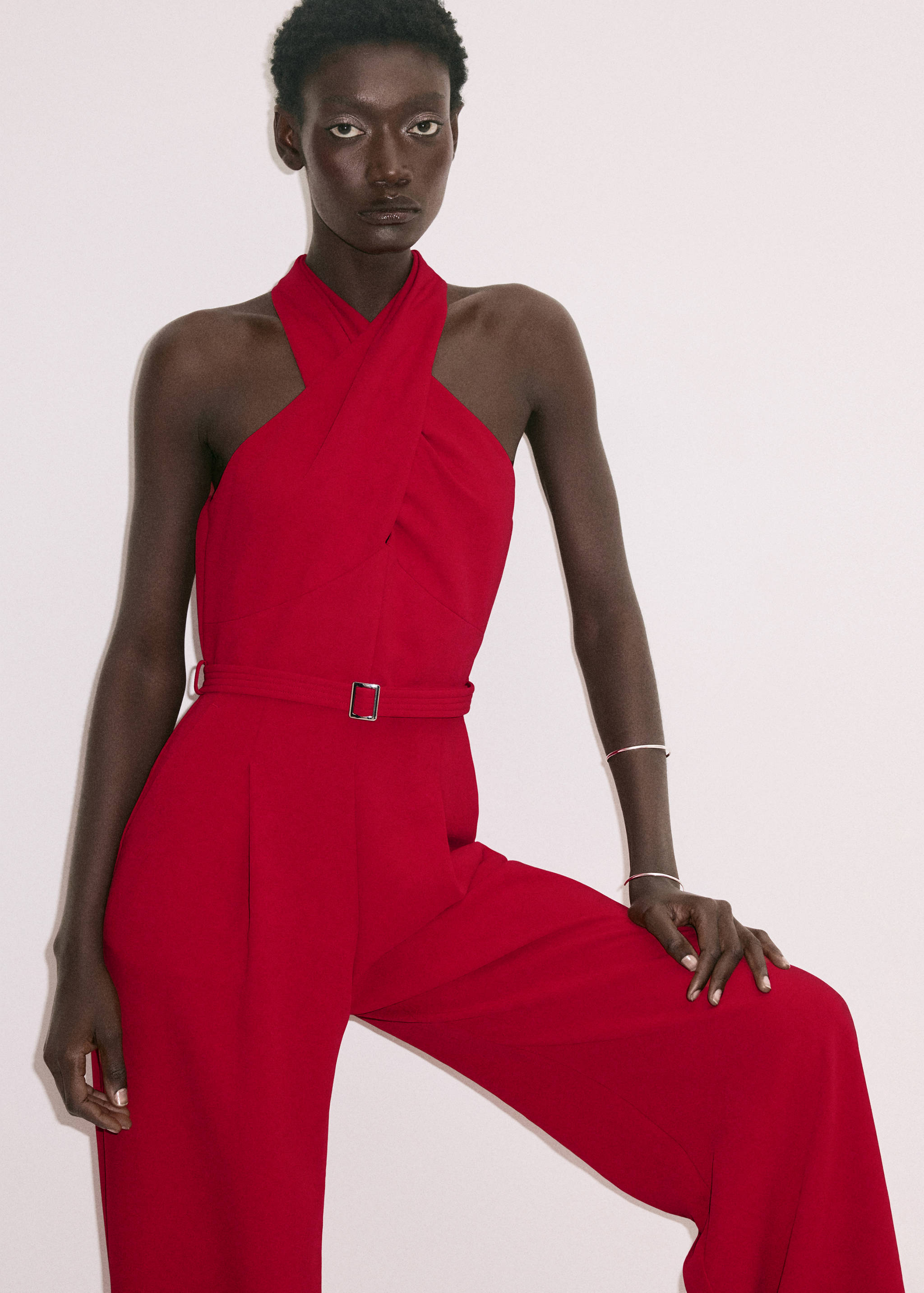 Red halter neck jumpsuit with a crossover strap bodice and a slim matching belt.
