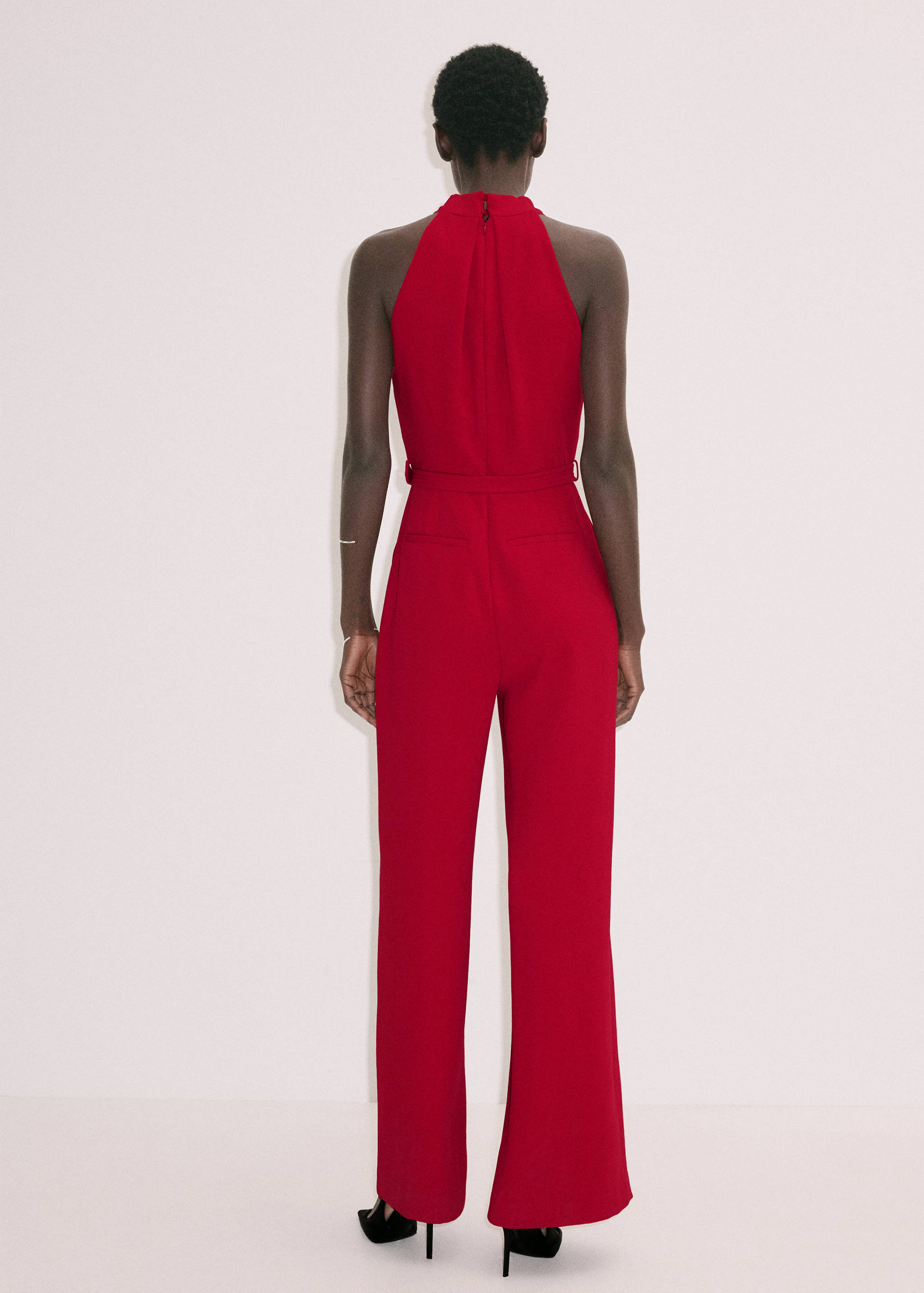 Red halter-neck jumpsuit shown from the back, featuring a fitted waist and straight trousers.