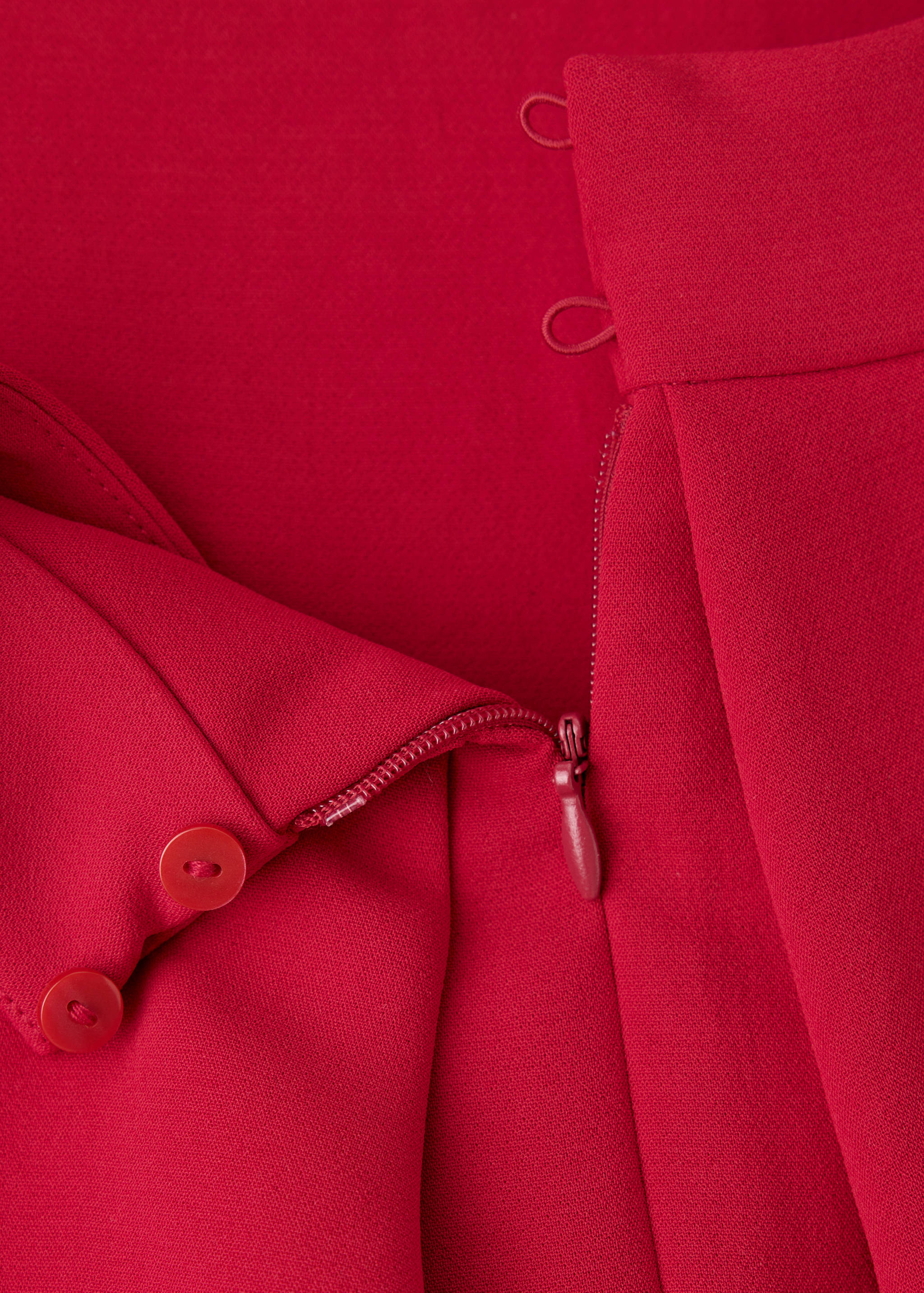 Red jumpsuit fabric detail showing zip and button closure.