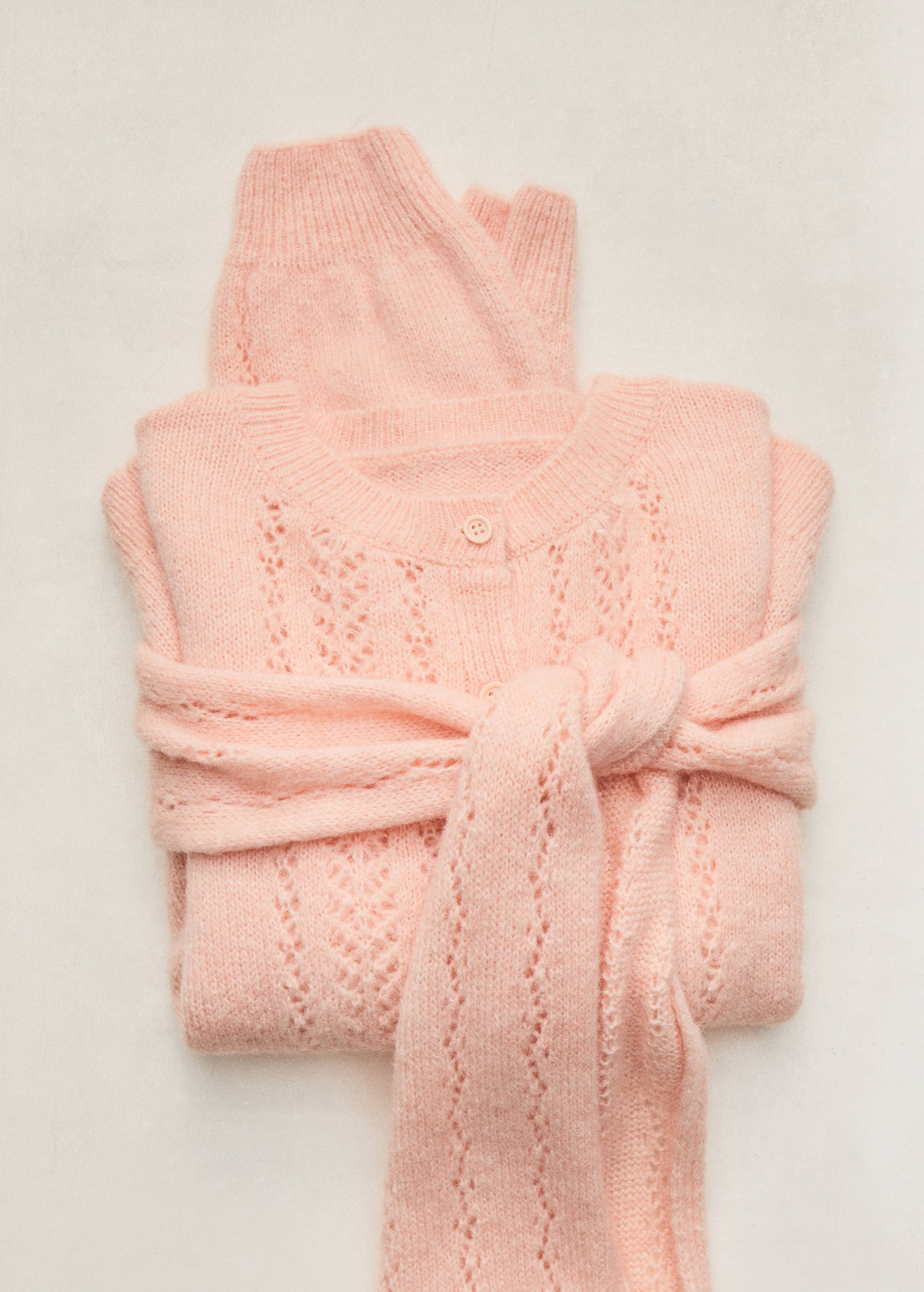 Pale pink knitted cardigan with pointelle pattern and tied sleeves.