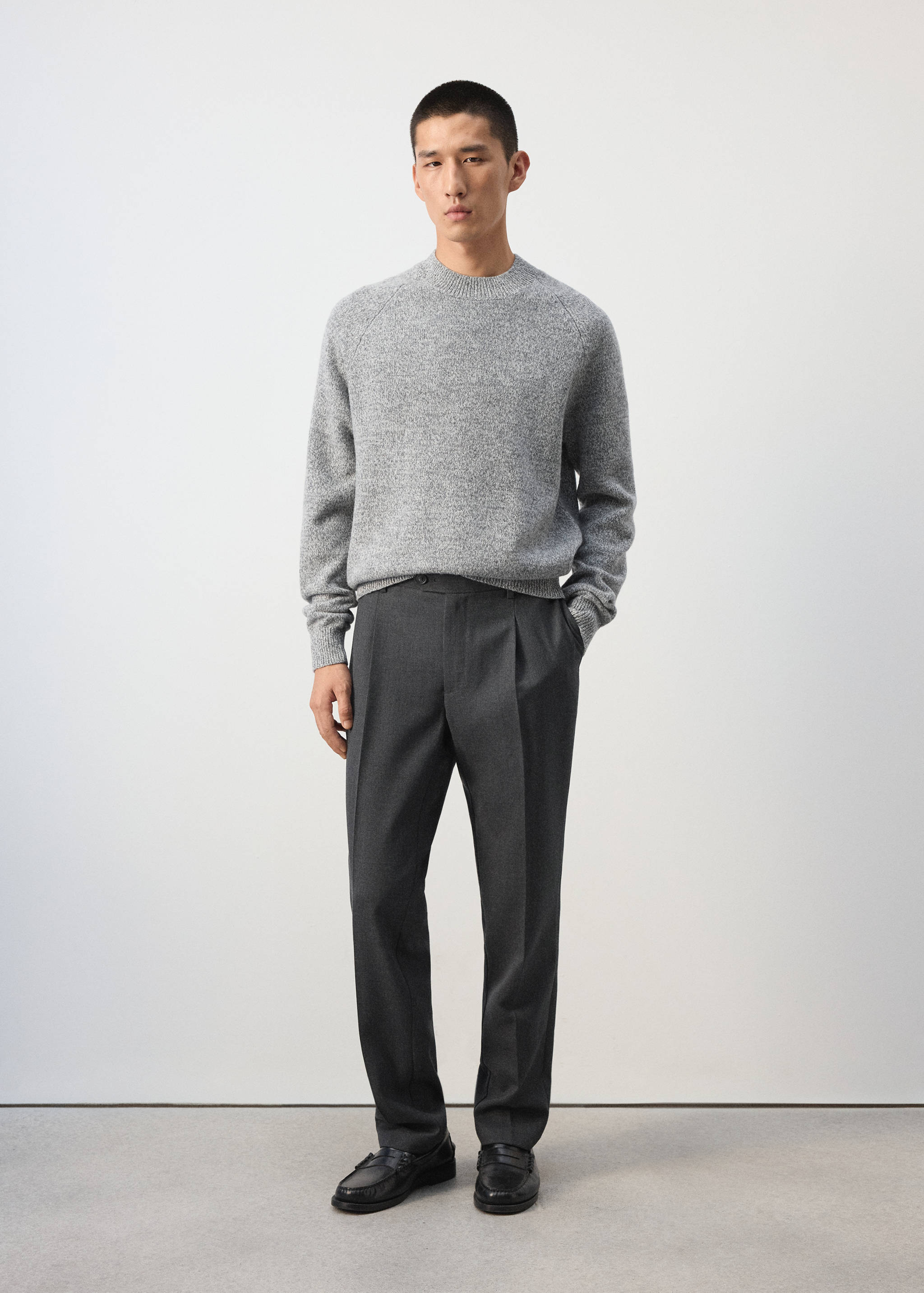 Grey melange knit sweater with a crew neck and long sleeves, worn with dark grey trousers.