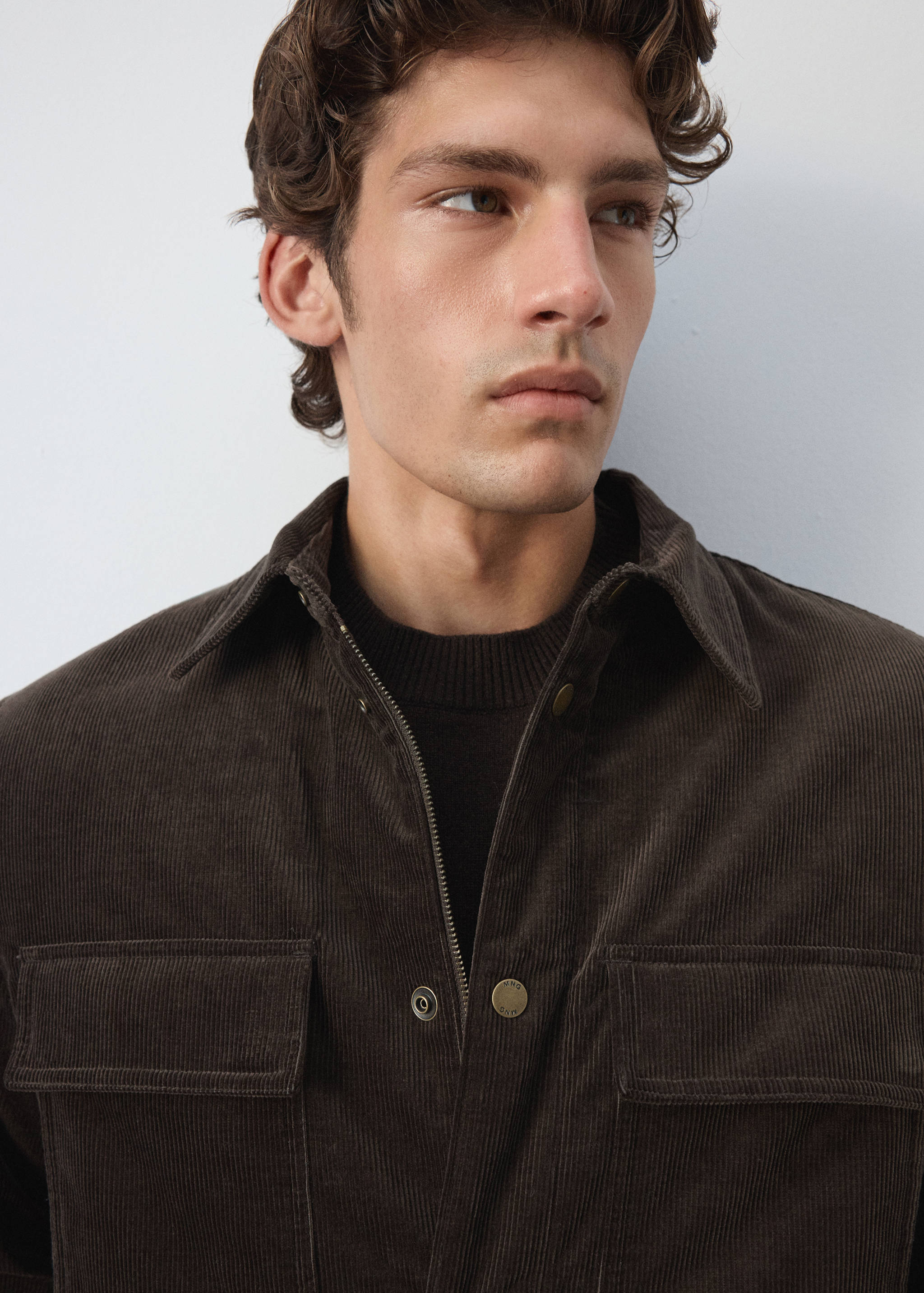 Close-up of a dark brown corduroy jacket with a collar and chest pockets.