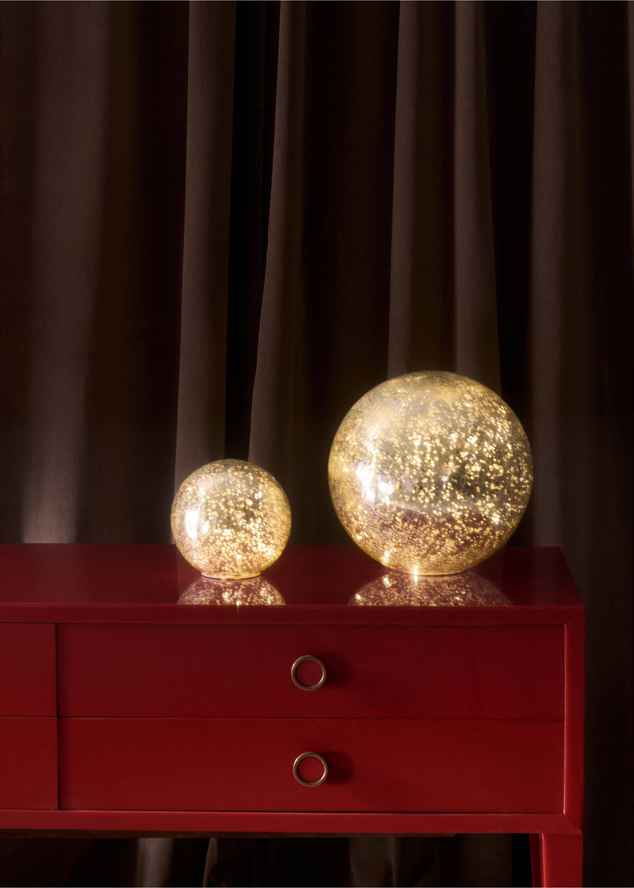 Two lit spherical Christmas decorations with a speckled glow on a red sideboard., Gold. Ref: 37027896-00.
