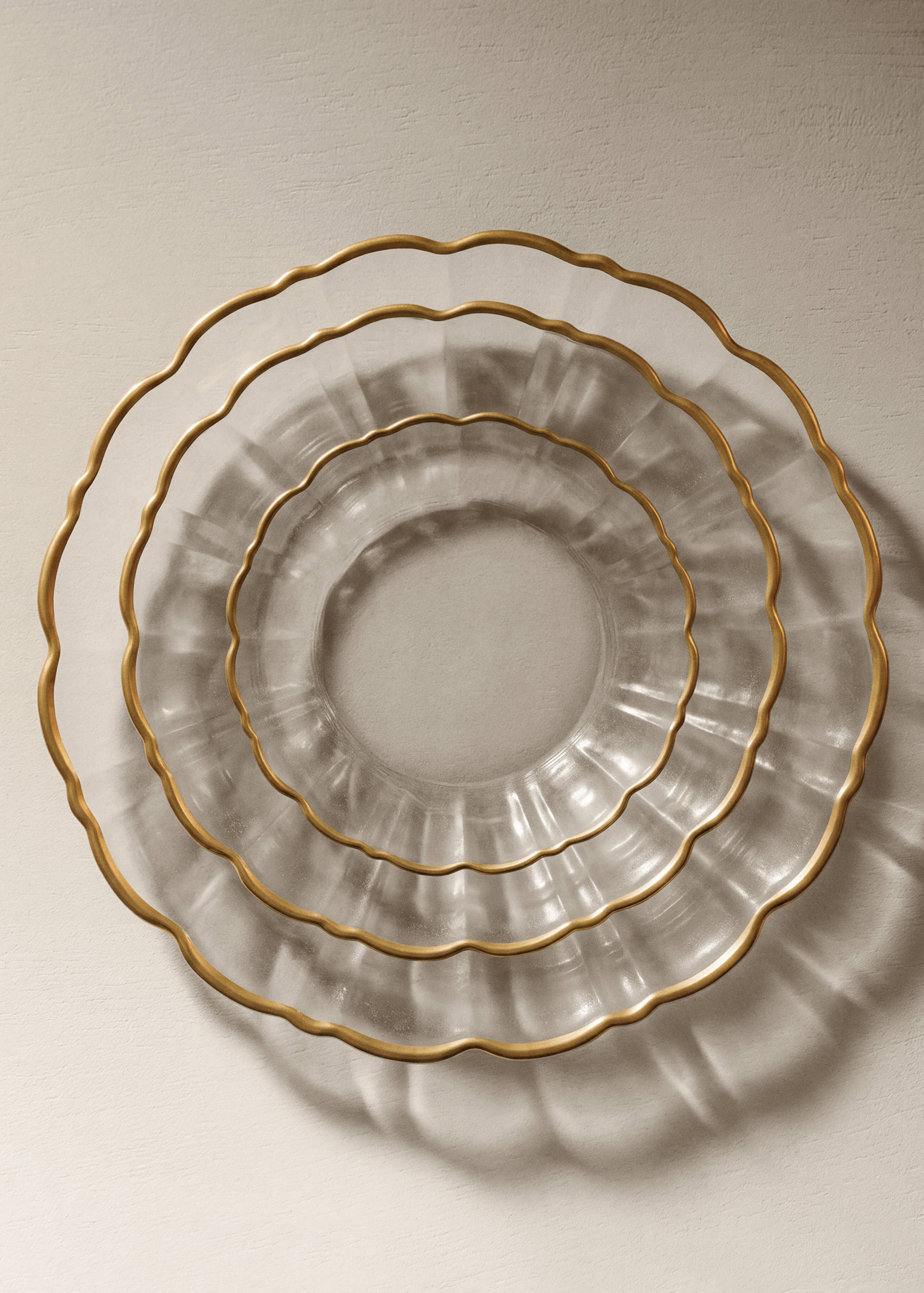 Three nested clear glass plates with scalloped edges and gold rims.