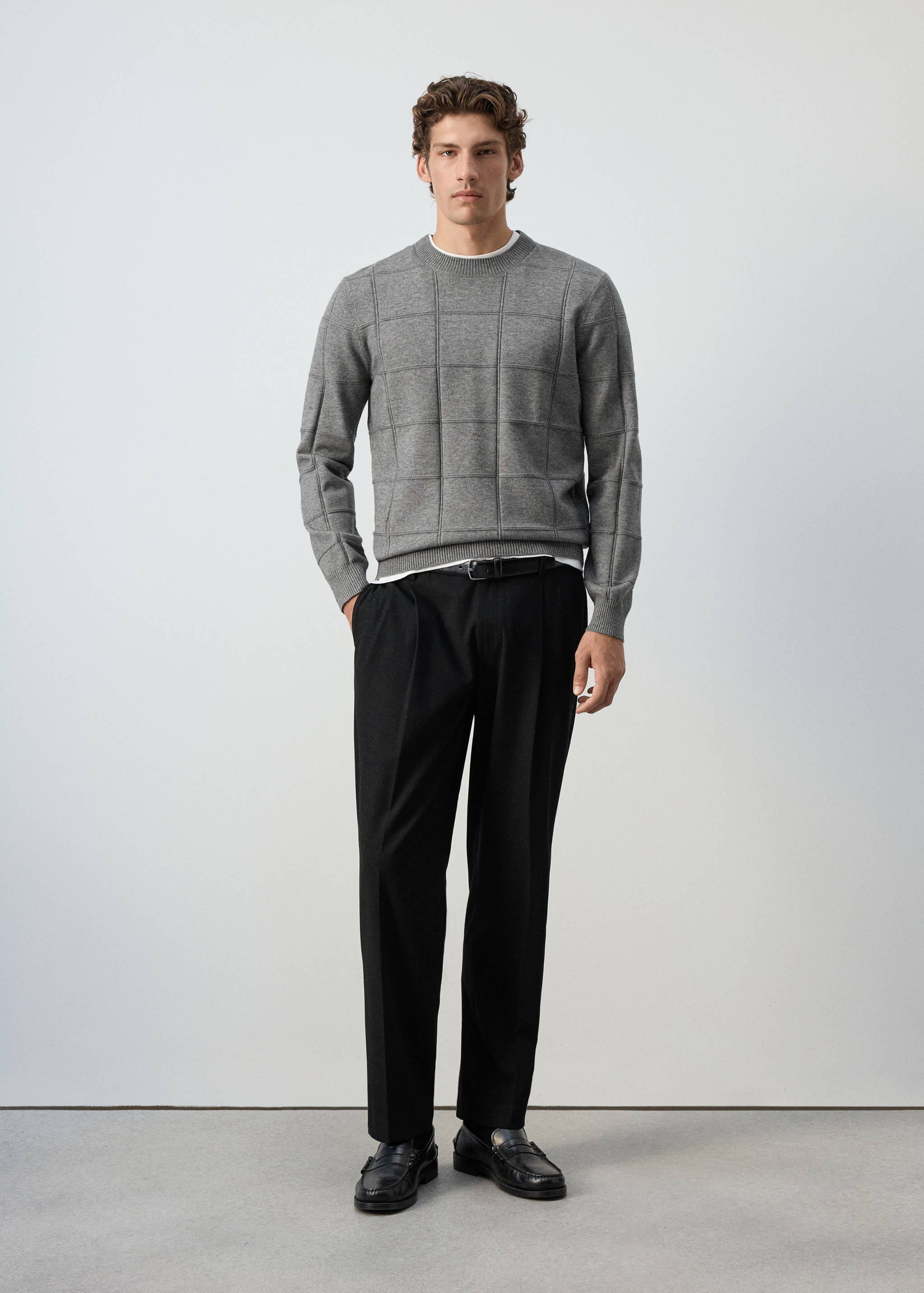 Grey crew neck jersey with a check pattern, worn with black trousers.