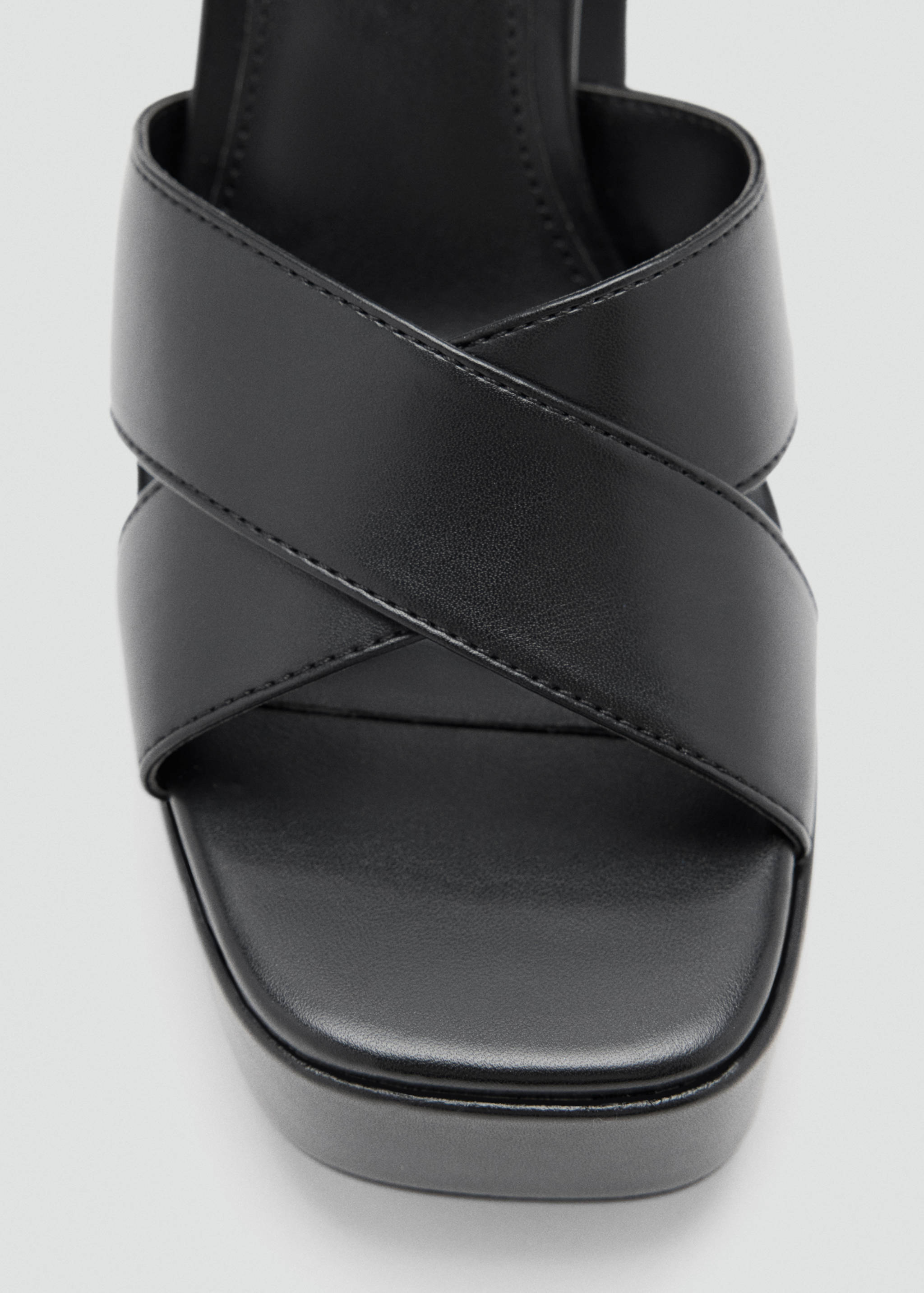 Close-up of a black sandal with crisscross straps and platform sole.