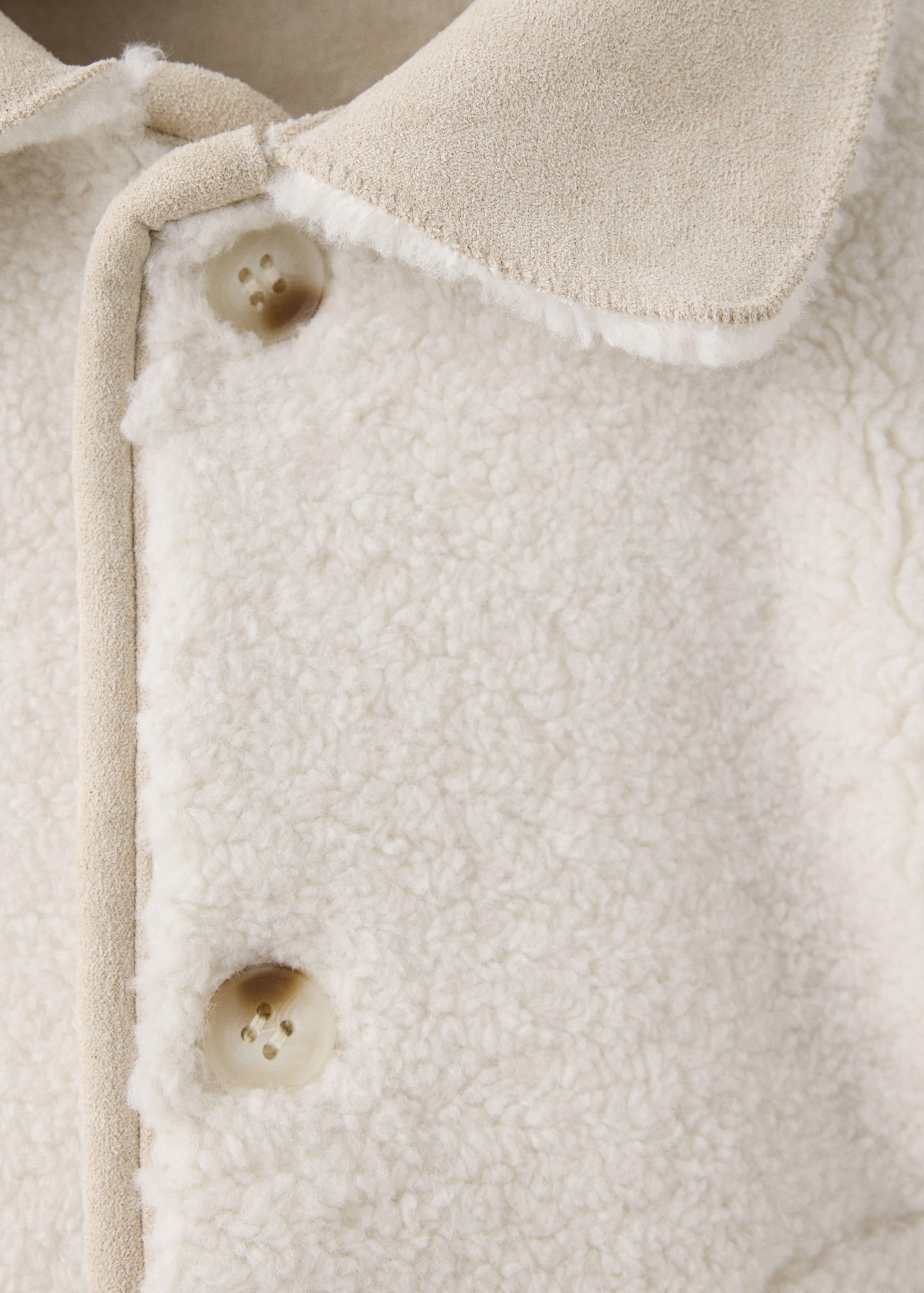 Close-up of an off-white fleece coat featuring a beige lapel collar and marbled buttons.