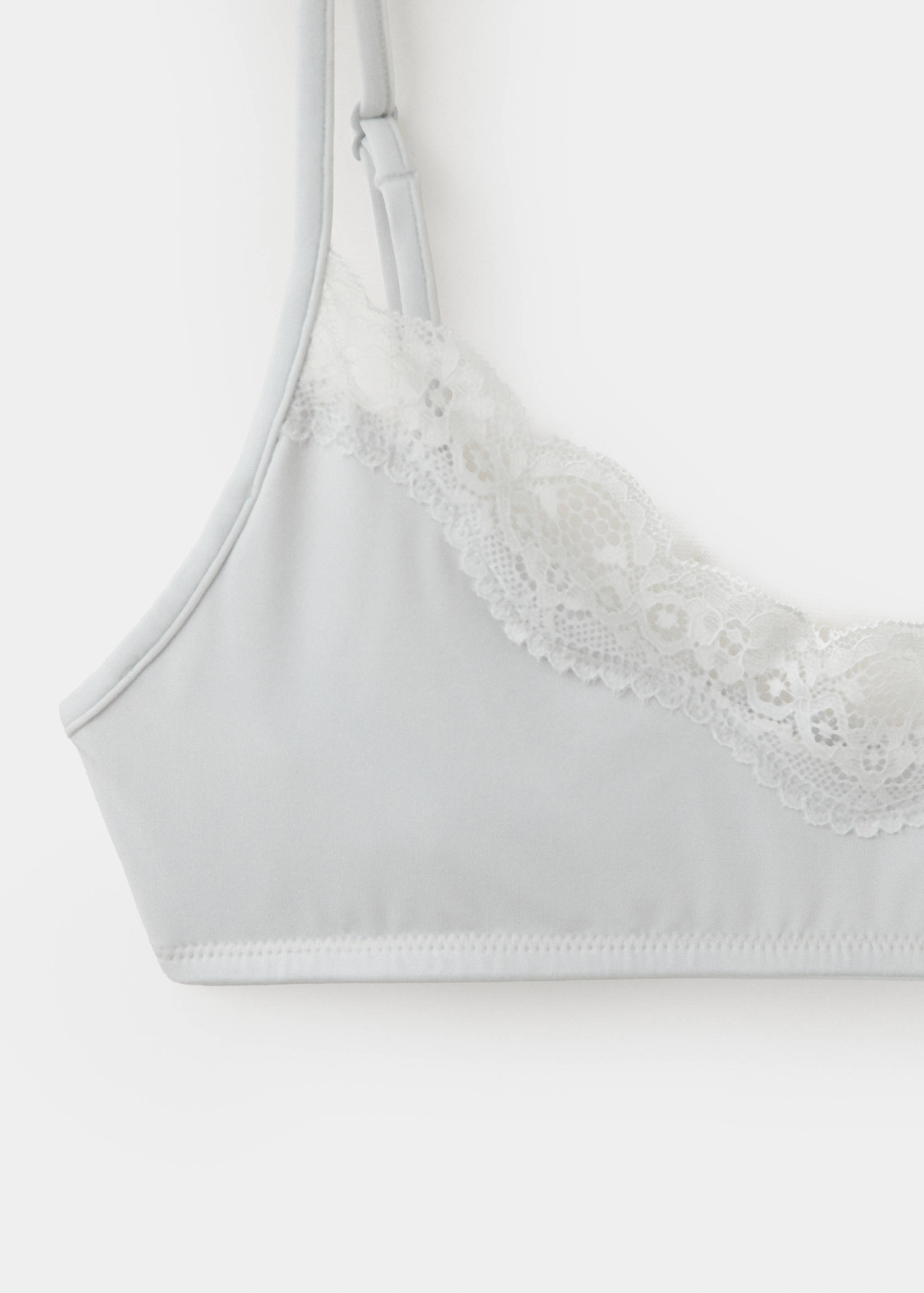 Close-up of a light grey bra with white lace trim and thin straps.