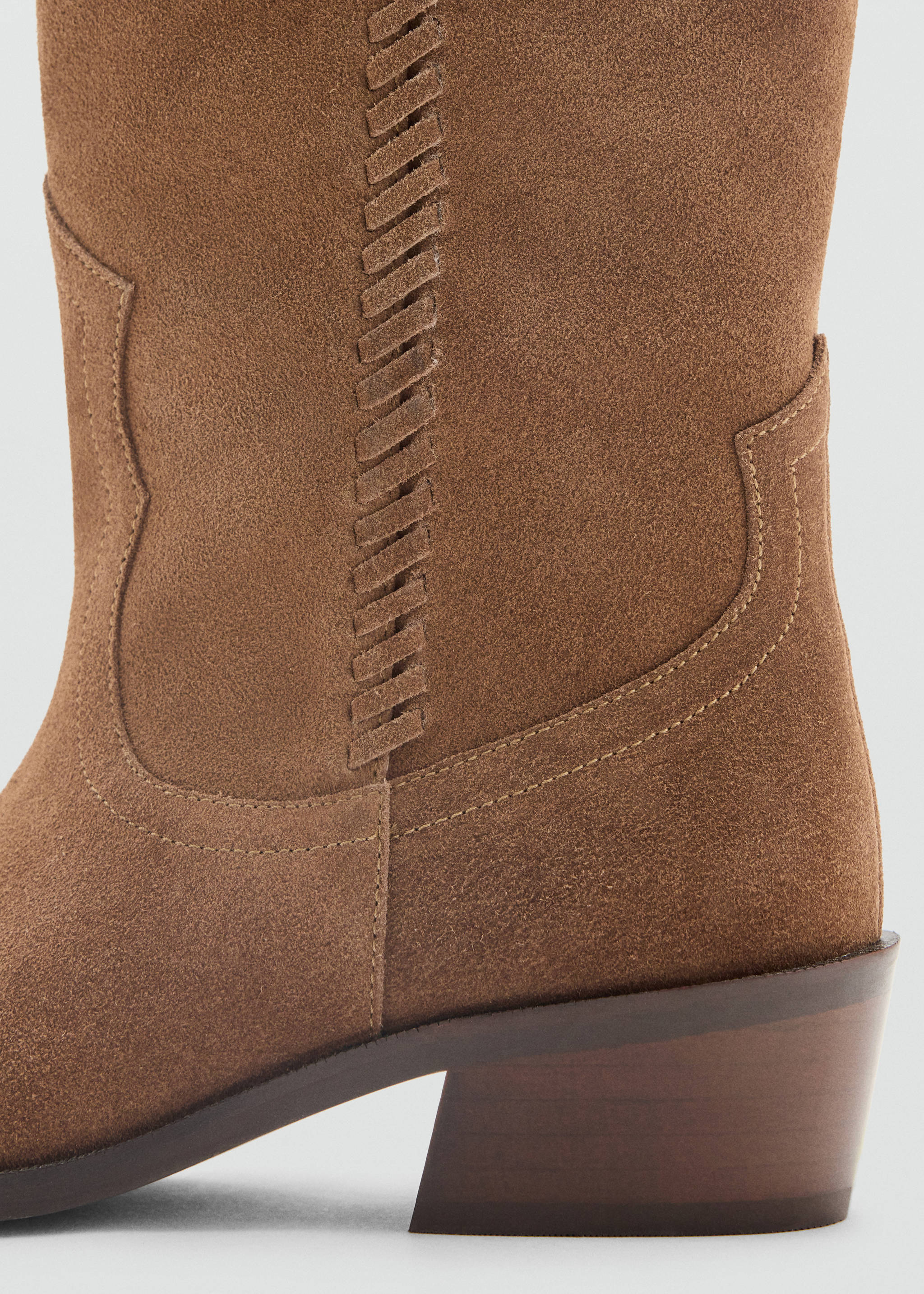 Brown suede boot detail showing whipstitch trim and stacked heel.