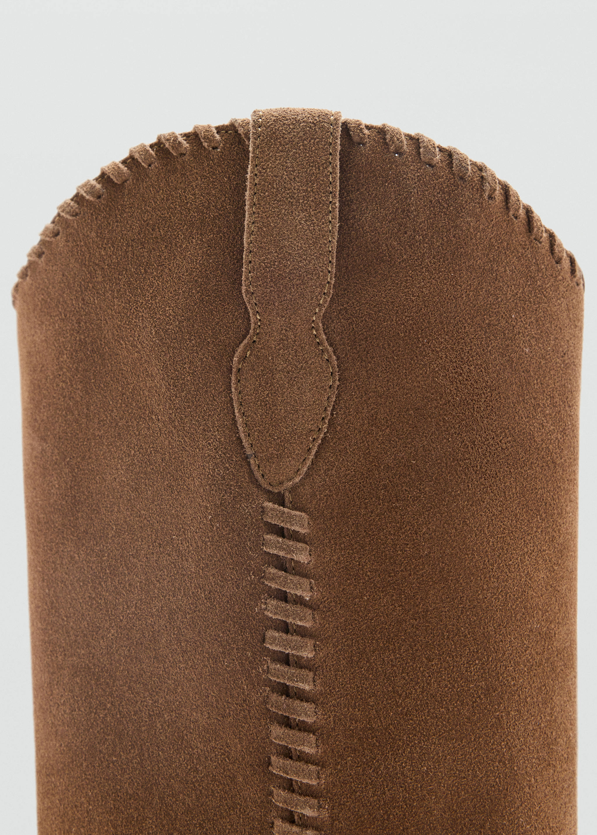Close-up of brown suede boot showing decorative whipstitch and pull tab detail.