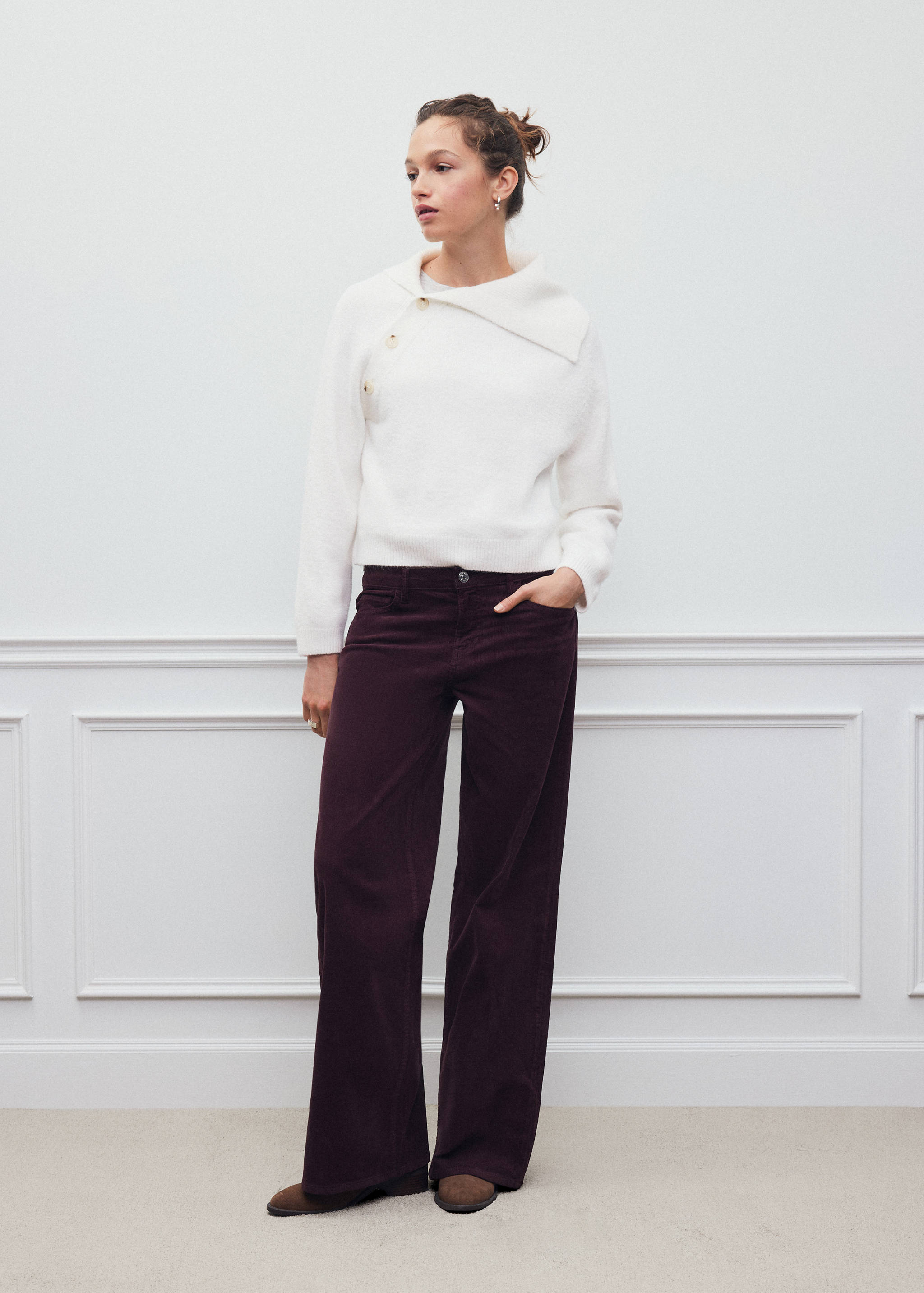 White textured jersey with an asymmetrical buttoned collar, worn with dark purple trousers.